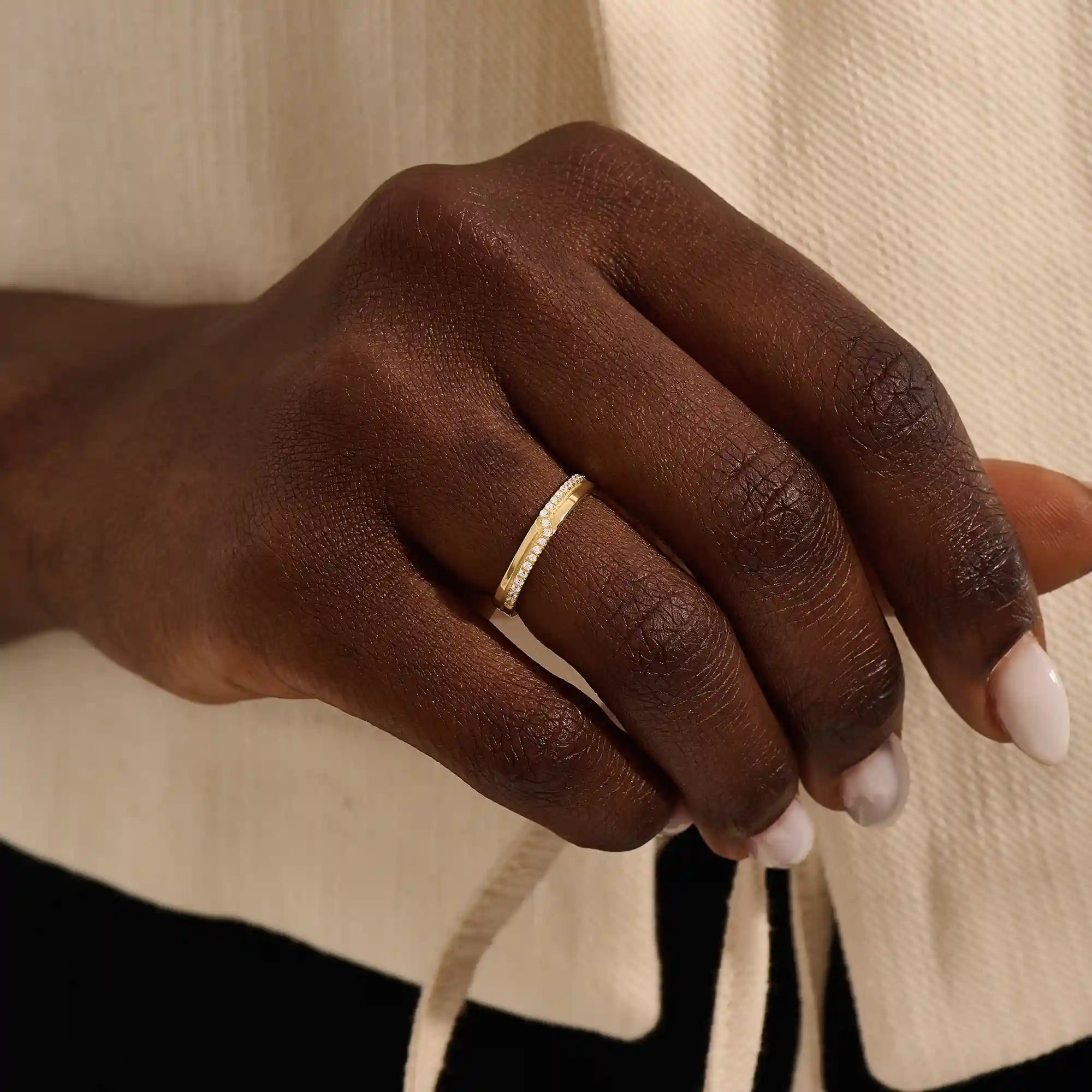 Close-up of a woman wearing a 14k solid yellow gold band with pointed chevron design and pavé set round brilliant cut moissanite stones, minimal and elegant wedding or stacking ring