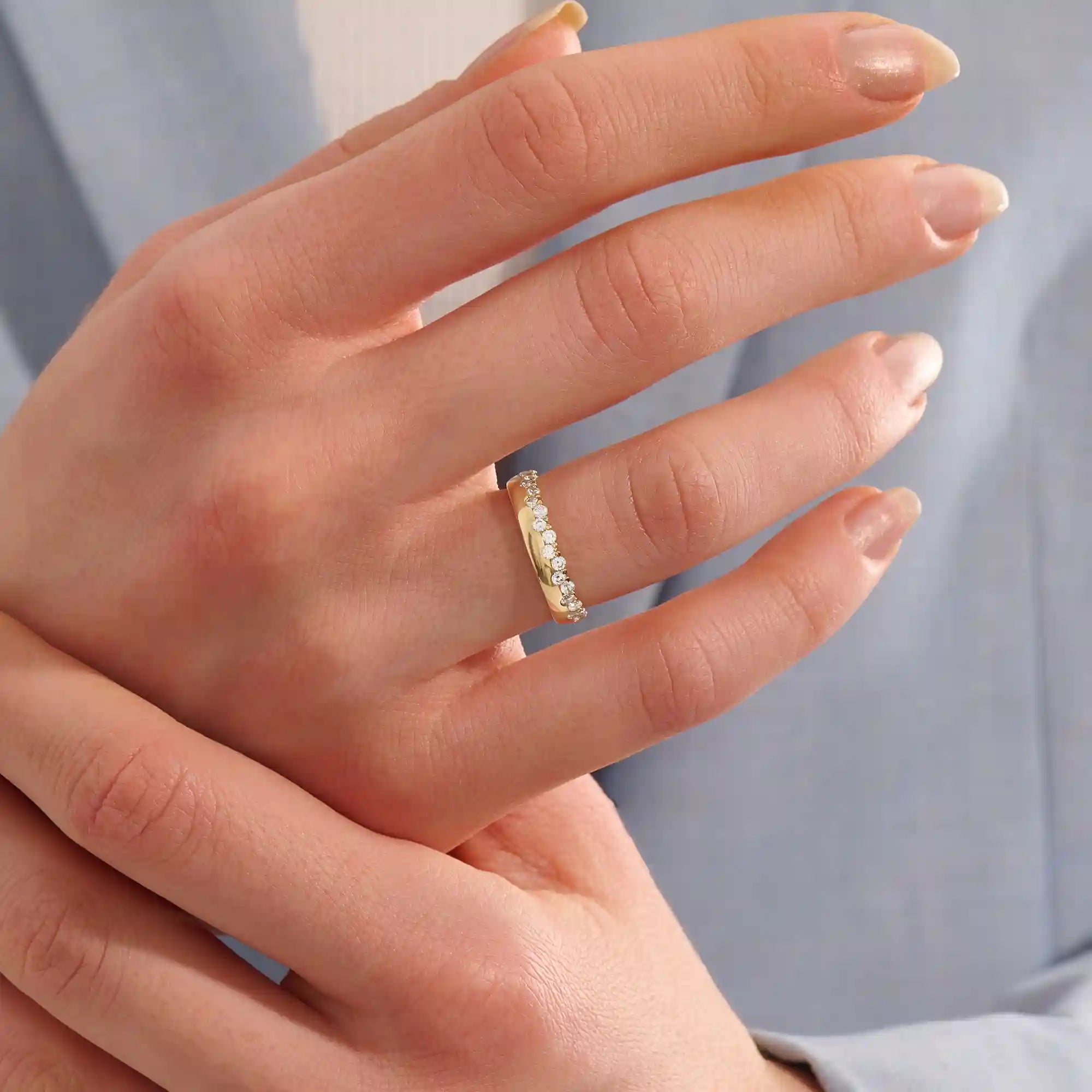 Close-up of a woman wearing a 14k solid yellow gold band with round brilliant cut moissanite stones in a single row and polished bead accents, elegant and timeless wedding jewelry