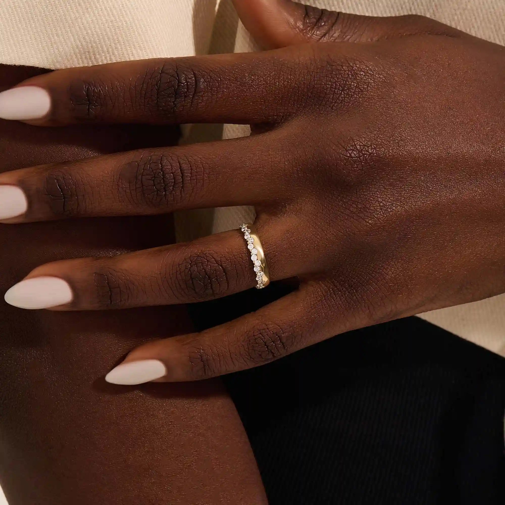 Close-up of a woman wearing a 14k solid yellow gold band with round brilliant cut moissanite stones in a single row and polished bead accents, elegant and timeless wedding jewelry
2
