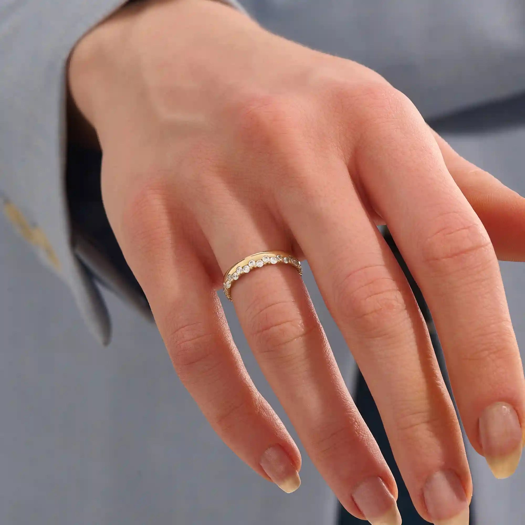 Close-up of a woman wearing a 14k solid yellow gold band with round brilliant cut moissanite stones in a single row and polished bead accents, elegant and timeless wedding jewelry