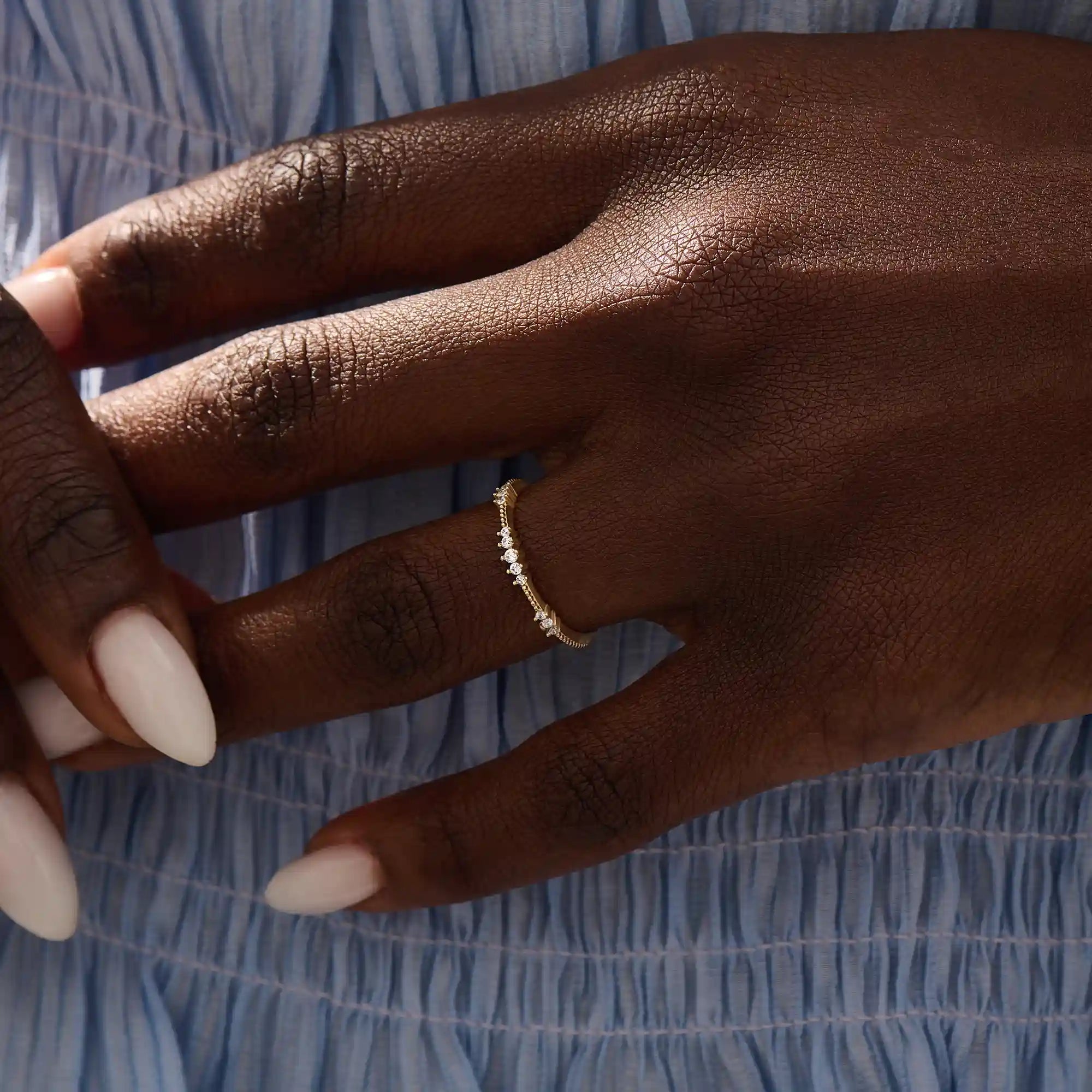 Close-up of a woman wearing a 14k solid yellow gold band with round brilliant cut moissanite stones in alternating prong and bead settings, minimal and elegant bridal jewelry