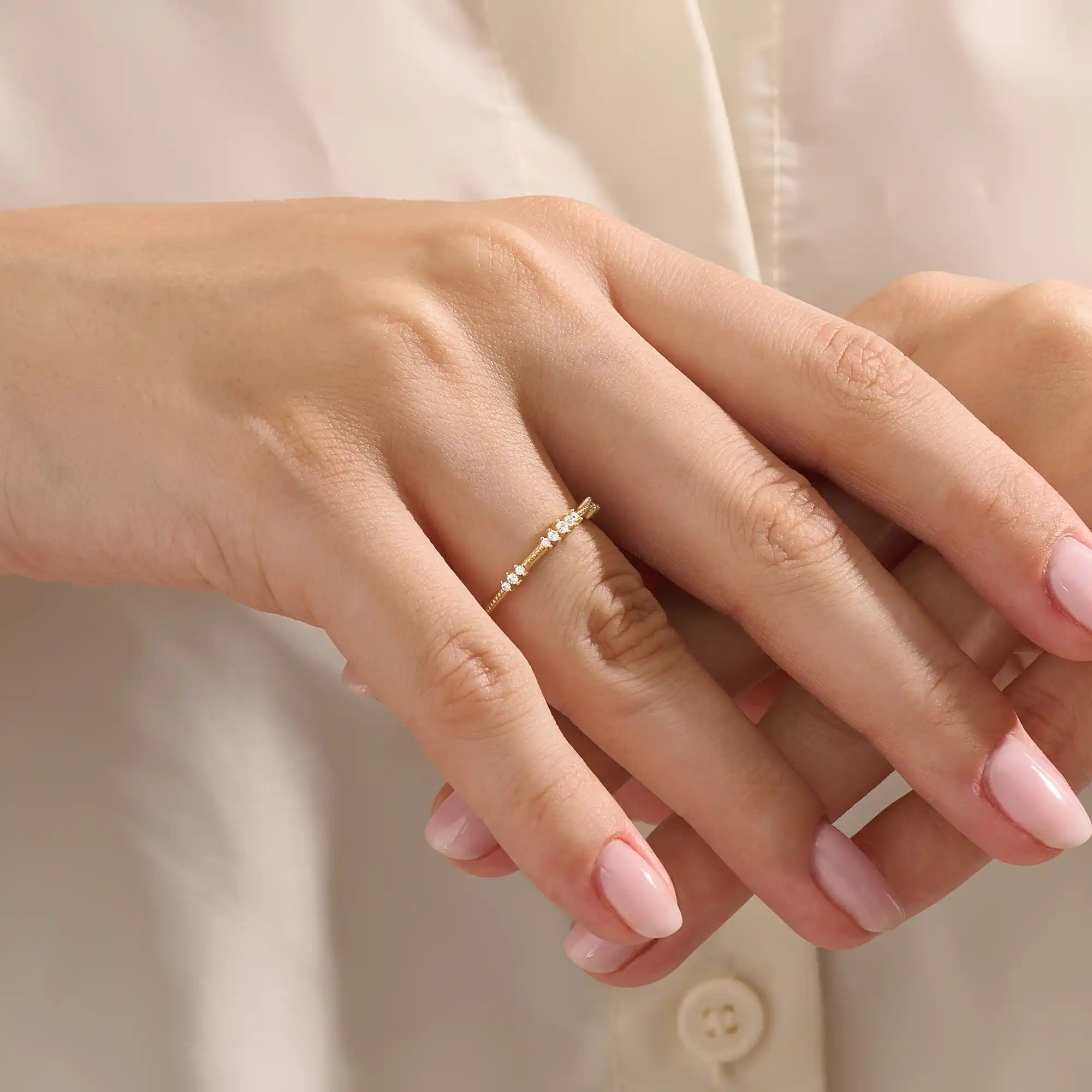 Close-up of a woman wearing a 14k solid yellow gold band with round brilliant cut moissanite stones in alternating prong and bead settings, minimal and elegant bridal jewelry