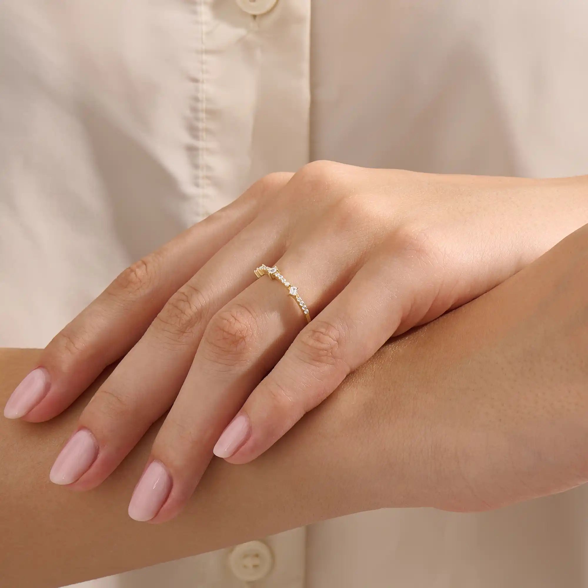Close-up of a woman wearing a 14k solid yellow gold band with three baguette cut moissanite stones and pavé set round moissanite accents, stylish and modern wedding or stacking ring