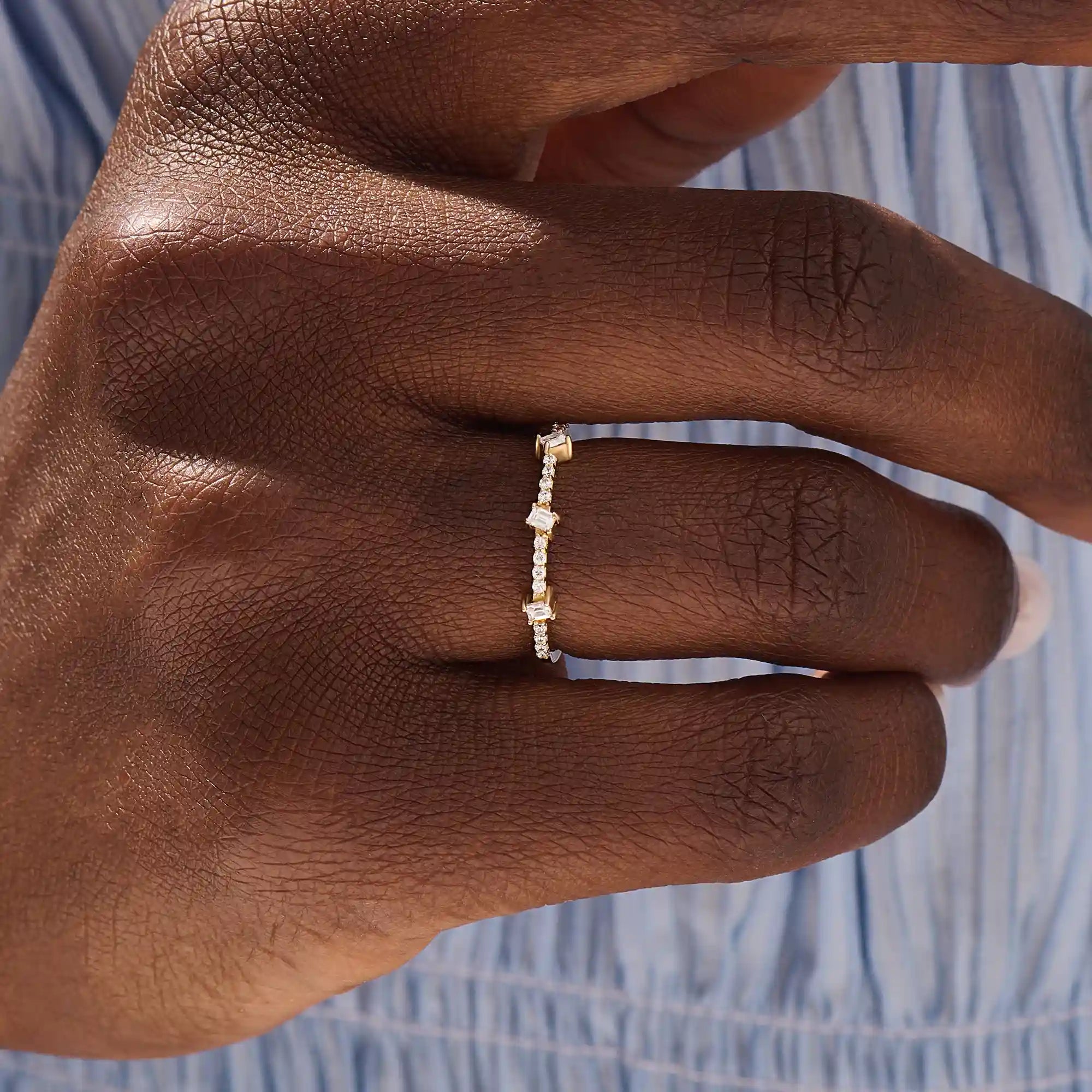 Close-up of a woman wearing a 14k solid yellow gold band with three baguette cut moissanite stones and pavé set round moissanite accents, stylish and modern wedding or stacking ring
3