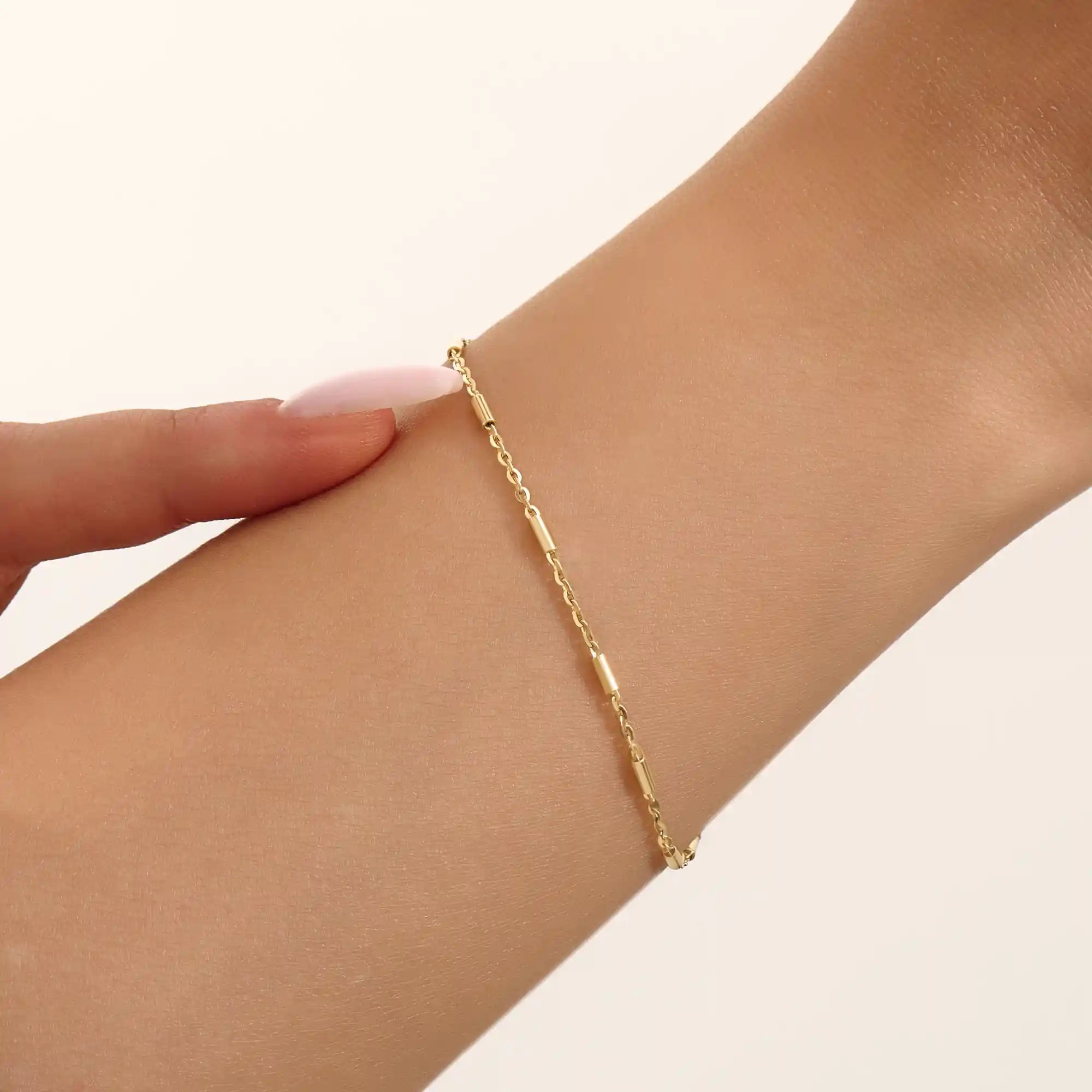 Close-up of a woman wearing a 14k solid yellow gold bar chain bracelet, its delicate design draping gracefully on the wrist for a refined everyday look.