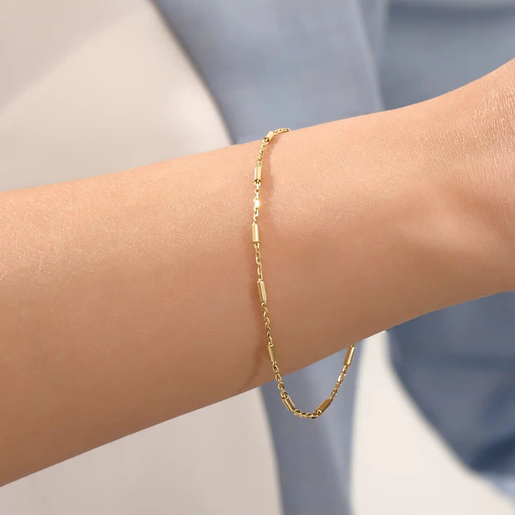 Close-up of a woman wearing a 14k solid yellow gold bar chain bracelet, its delicate design draping gracefully on the wrist for a refined everyday look.