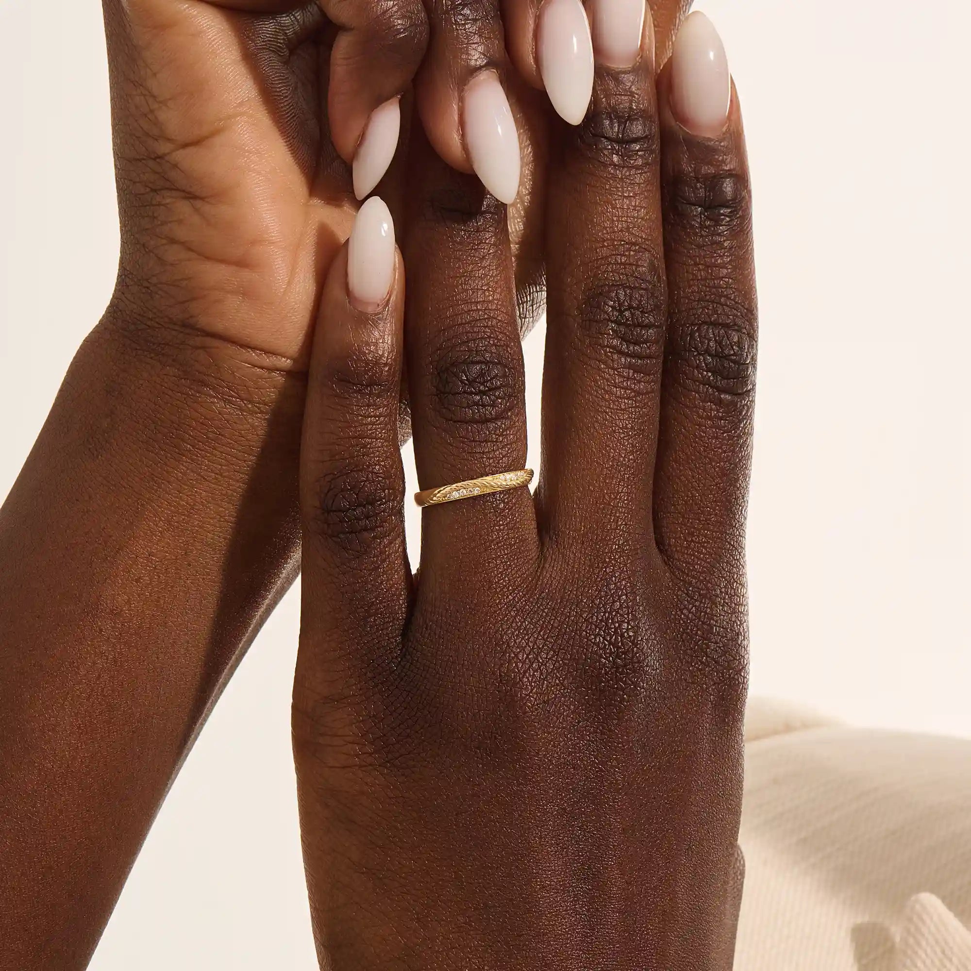 Close-up of a woman wearing a 14k solid yellow gold braided wedding band with a row of round diamonds, elegant and understated style