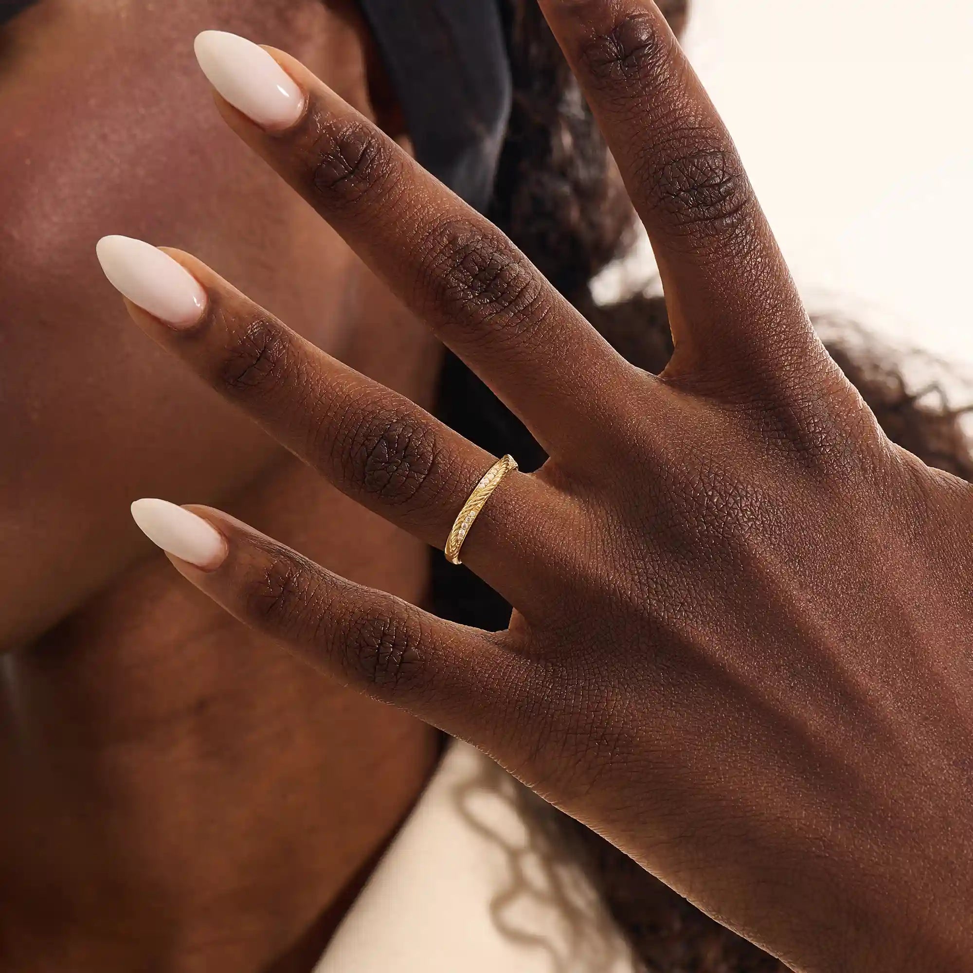 Close-up of a woman wearing a 14k solid yellow gold braided wedding band with a row of round diamonds, elegant and understated style