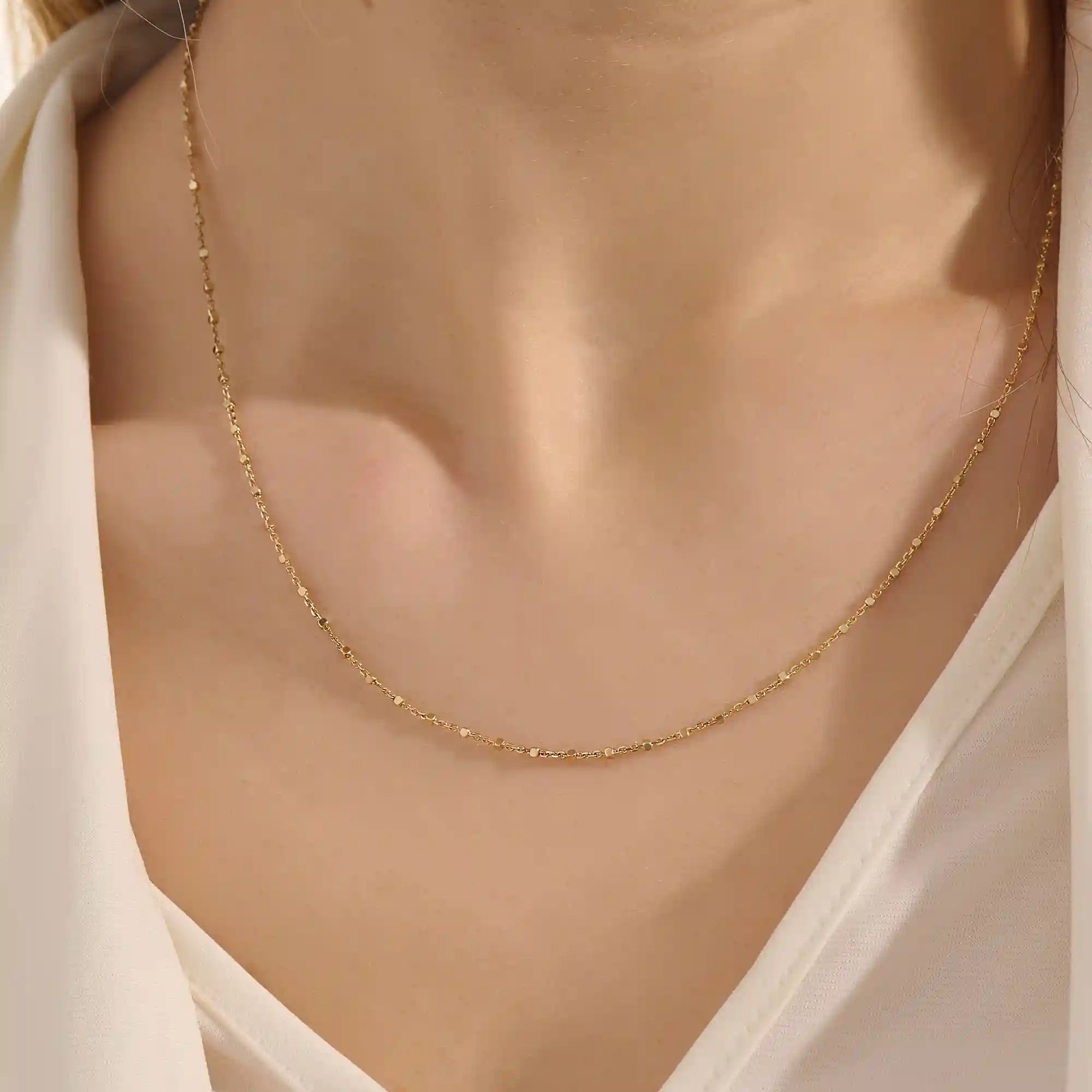 Close-up of a woman wearing a 14k solid yellow gold dot chain necklace with evenly spaced flat square links, styled alone for a simple, modern statement.