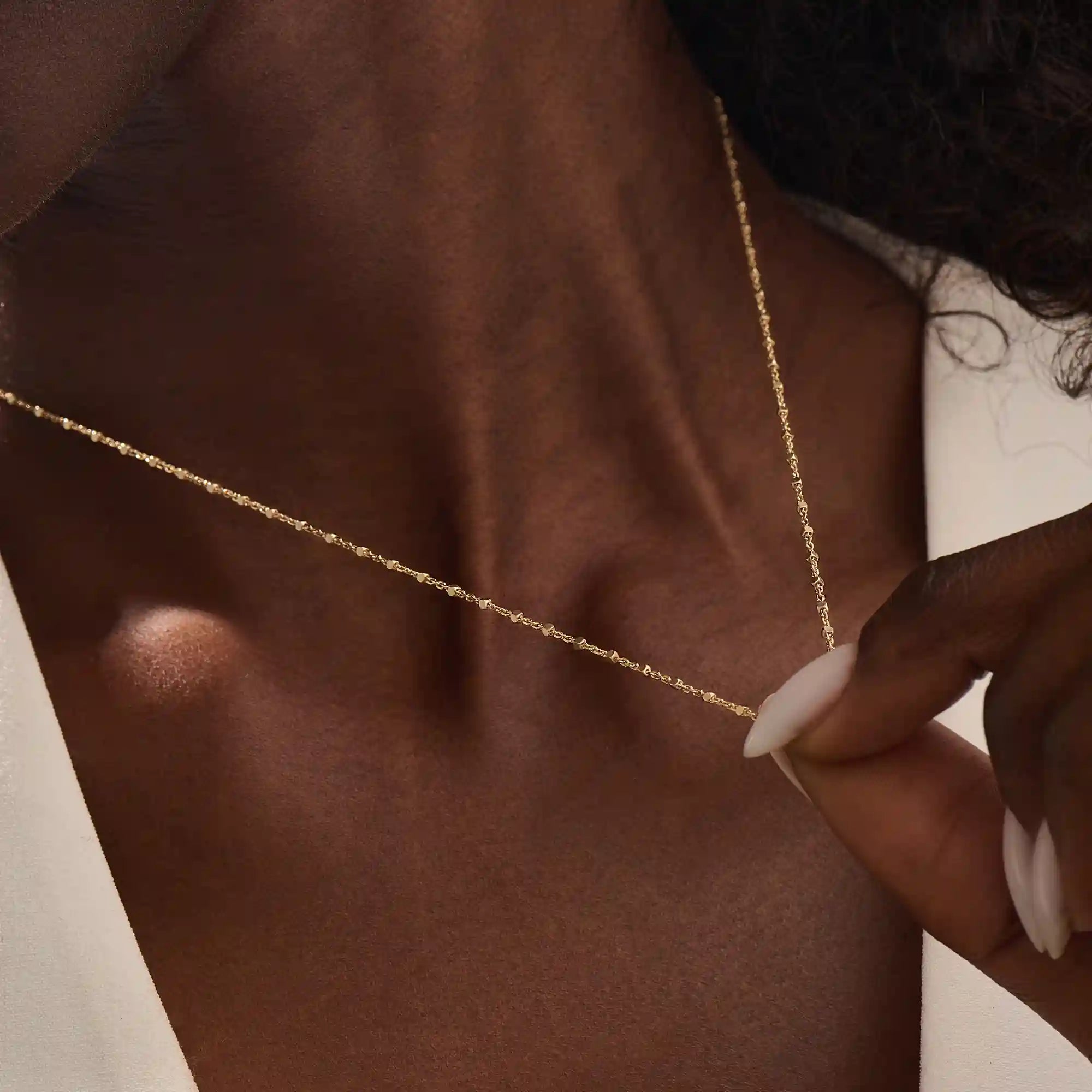 Close-up of a woman wearing a 14k solid yellow gold dot chain necklace with evenly spaced flat square links, styled alone for a simple, modern statement.
