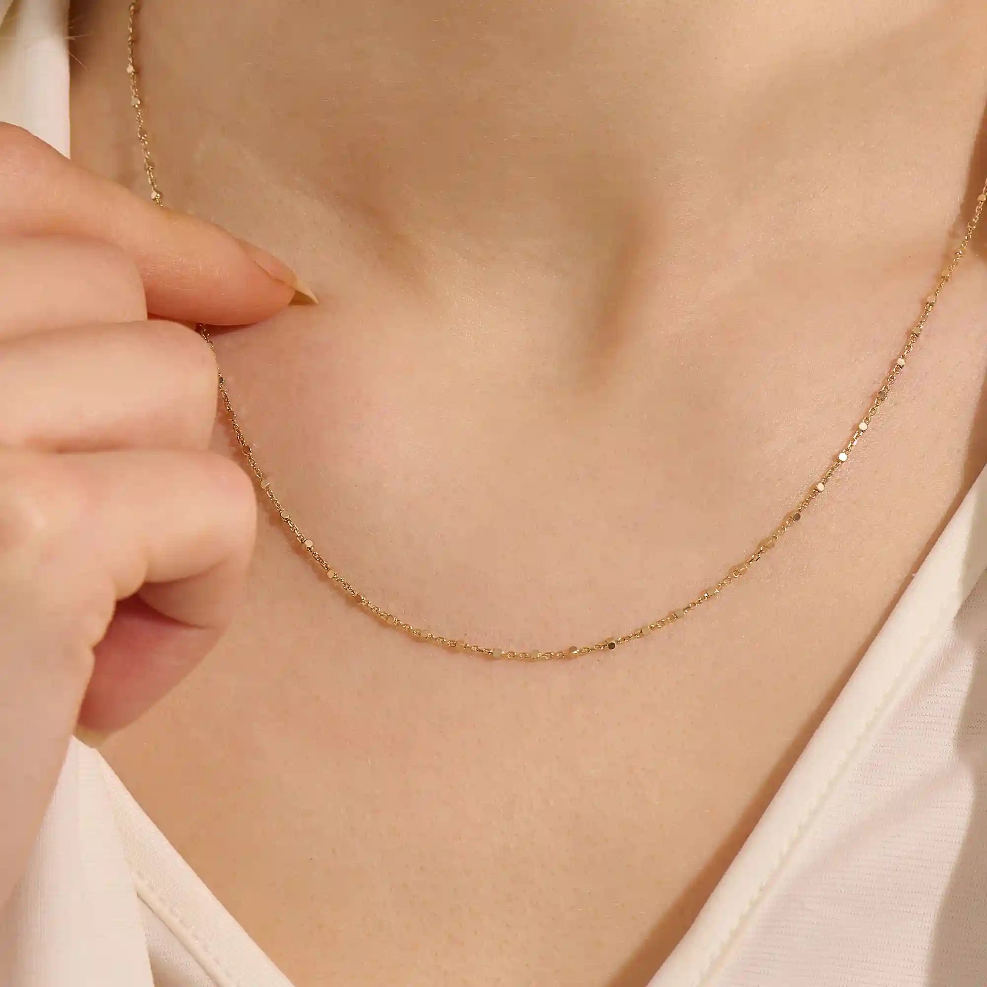 Close-up of a woman wearing a 14k solid yellow gold dot chain necklace with evenly spaced flat square links, styled alone for a simple, modern statement.