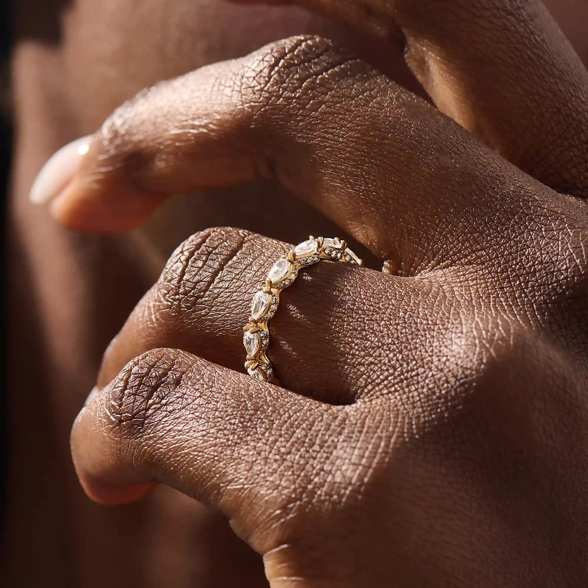 Close-up of a woman wearing a 14k solid yellow gold eternity band with sideways pear cut moissanite stones and pavé set round moissanite accents, ornate and elegant wedding jewelry