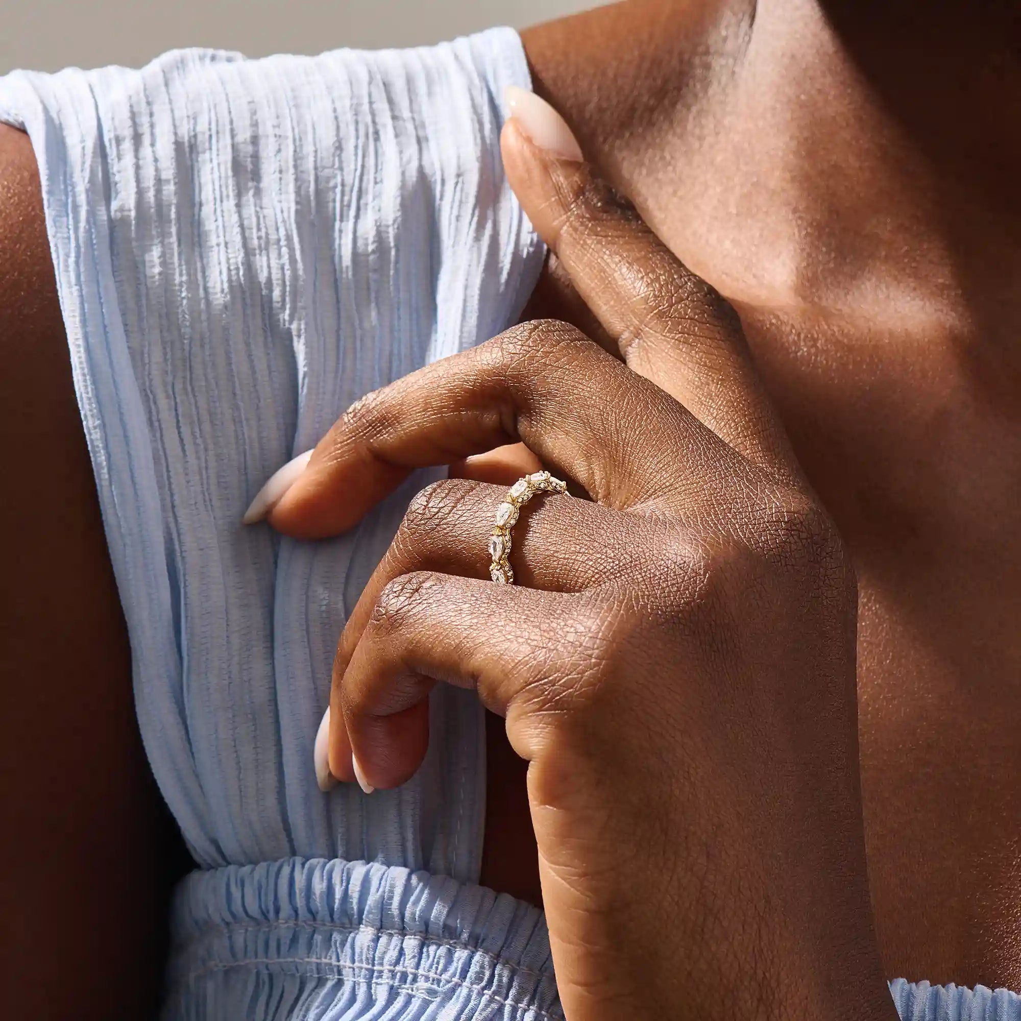 Close-up of a woman wearing a 14k solid yellow gold eternity band with sideways pear cut moissanite stones and pavé set round moissanite accents, ornate and elegant wedding jewelry