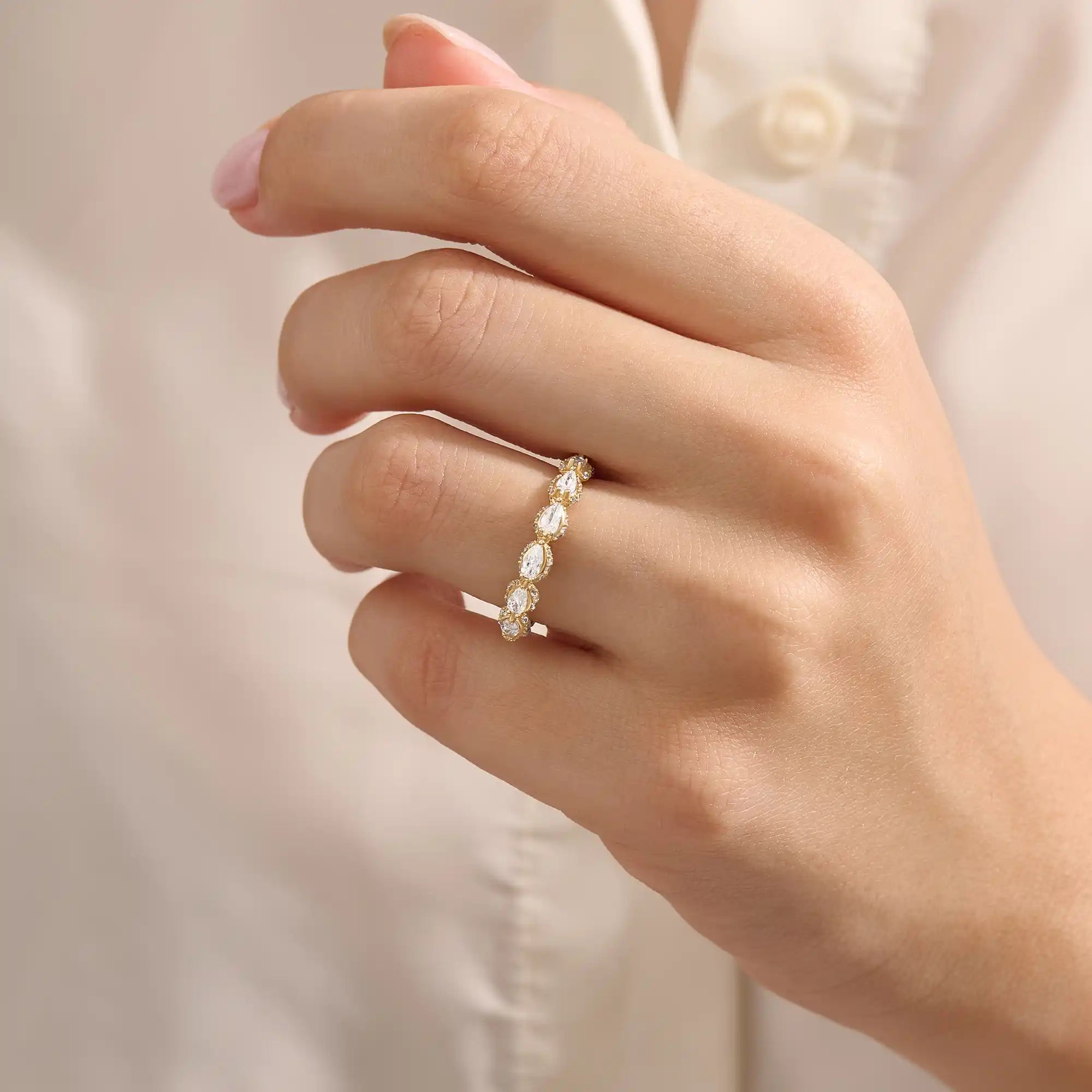 Close-up of a woman wearing a 14k solid yellow gold eternity band with sideways pear cut moissanite stones and pavé set round moissanite accents, ornate and elegant wedding jewelry