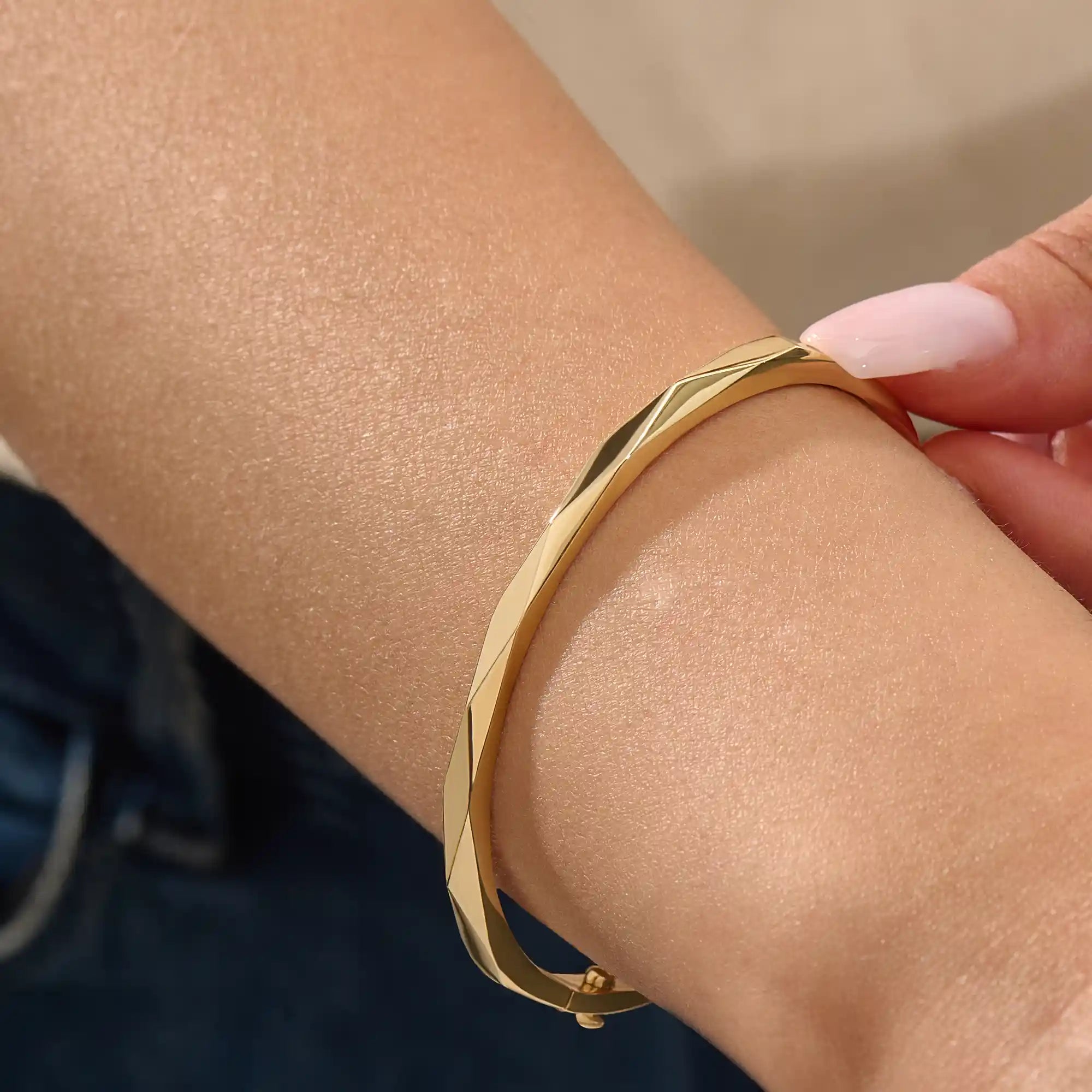 Close-up of a woman wearing a 14k solid yellow gold faceted bangle bracelet, showing the bracelet’s subtle geometric texture and reflective shine on the wrist.