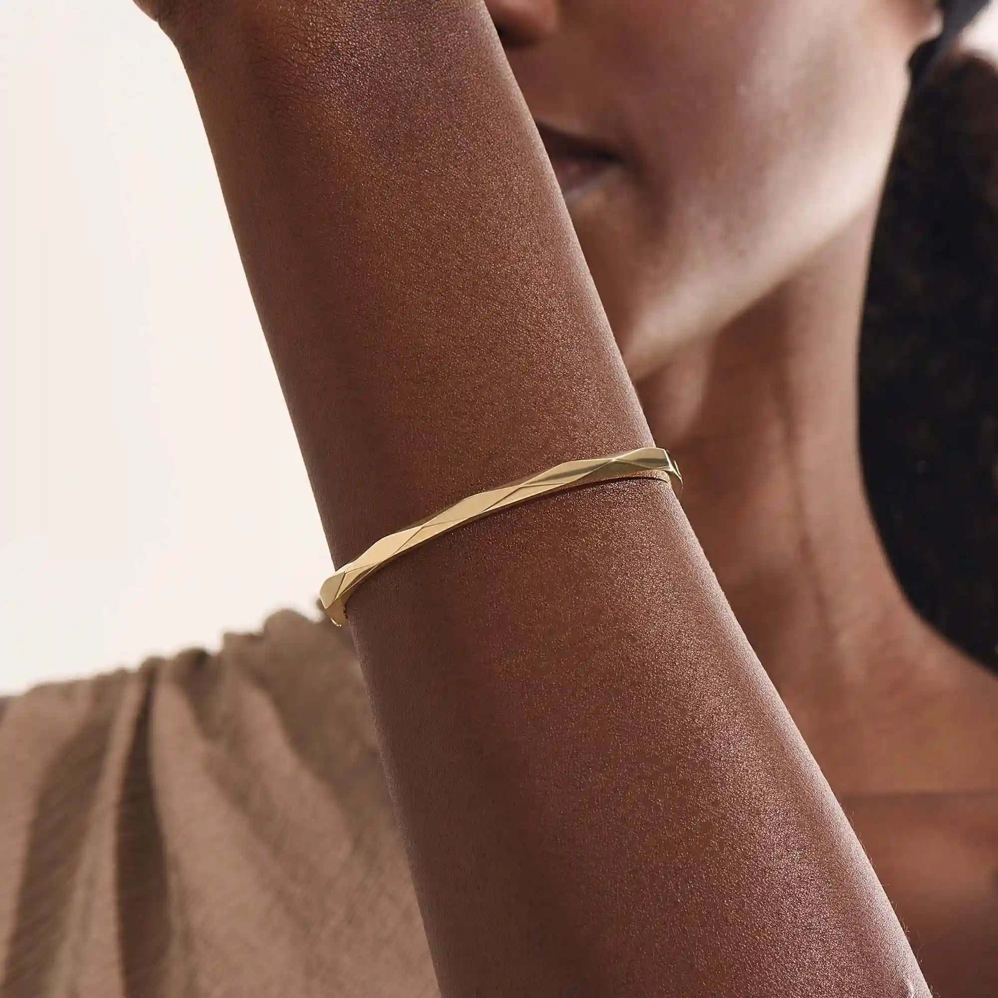 Close-up of a woman wearing a 14k solid yellow gold faceted bangle bracelet, showing the bracelet’s subtle geometric texture and reflective shine on the wrist.