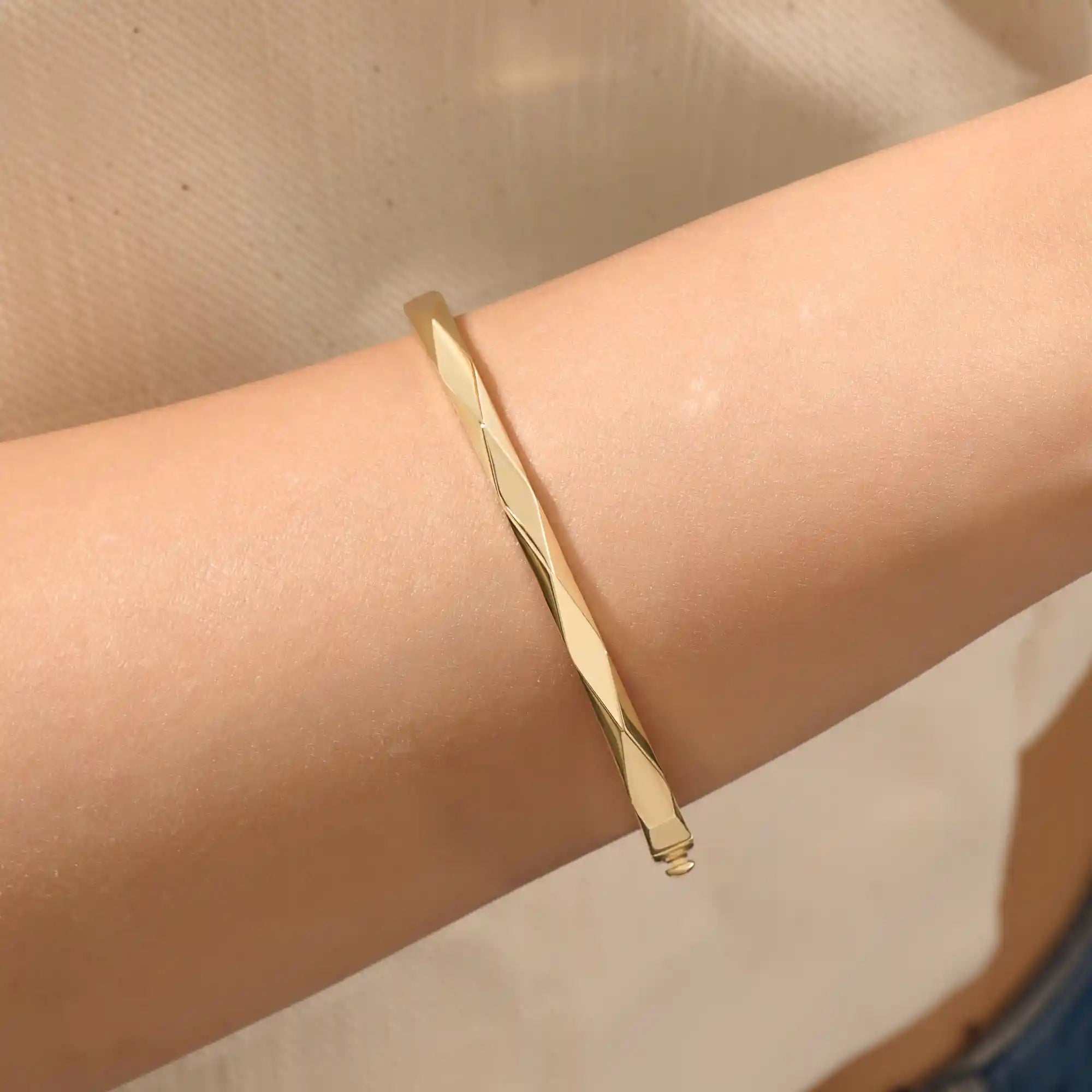 Close-up of a woman wearing a 14k solid yellow gold faceted bangle bracelet, showing the bracelet’s subtle geometric texture and reflective shine on the wrist.