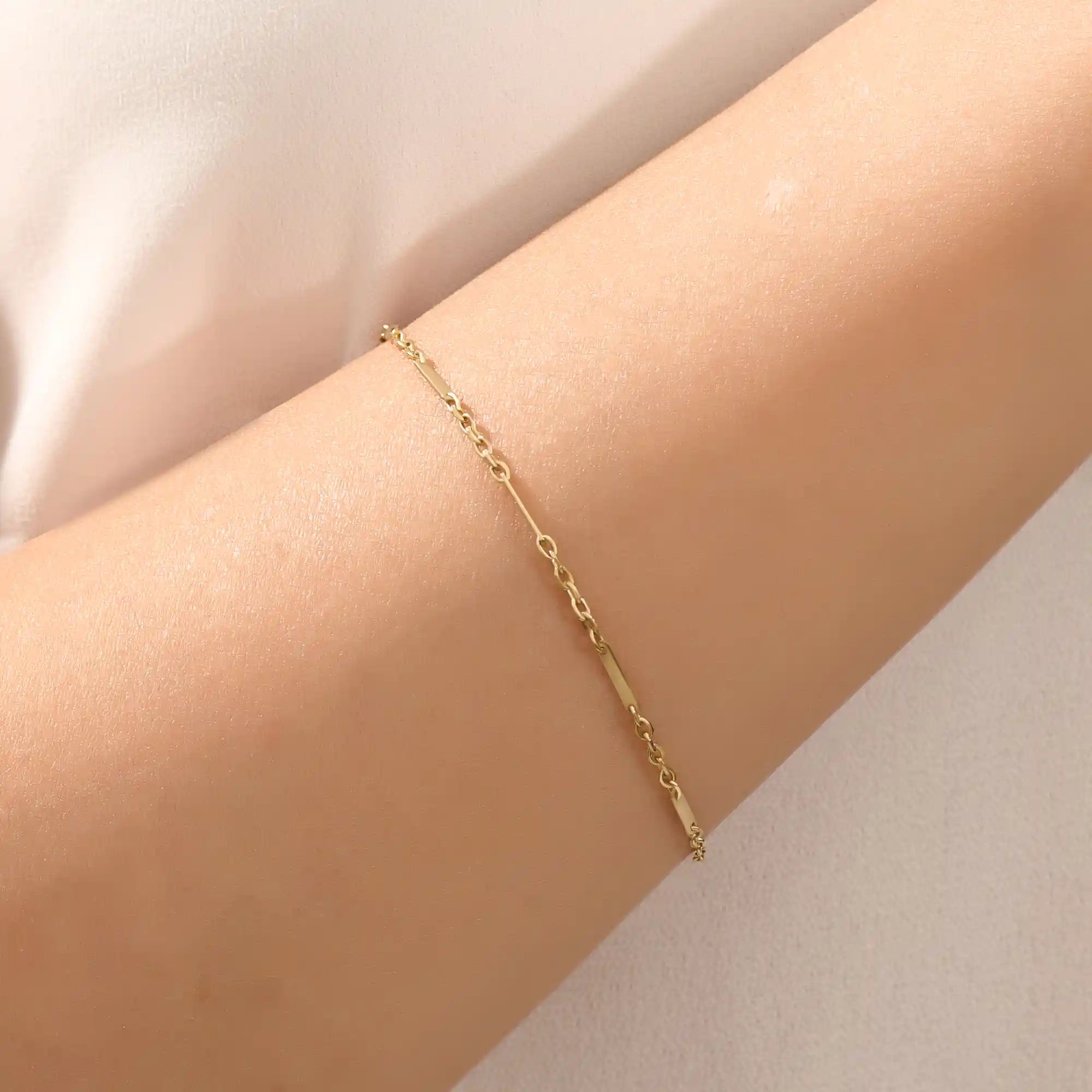 Close-up of a woman wearing a 14k solid yellow gold flat bar chain bracelet, the delicate design draping elegantly across the wrist for a timeless minimalist look.
