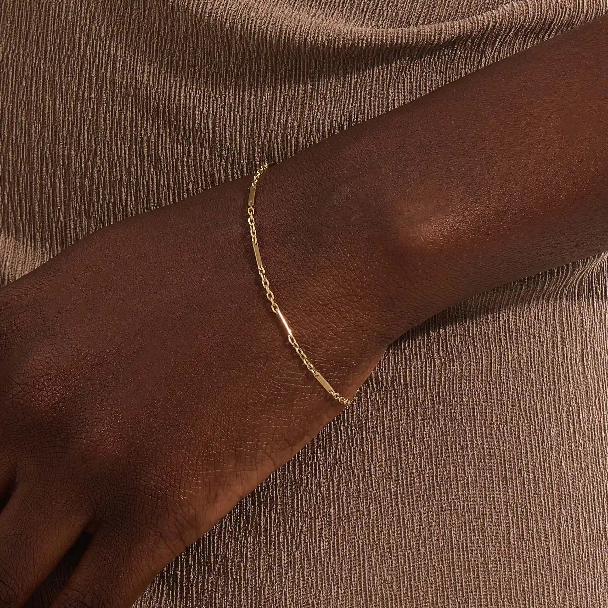 Close-up of a woman wearing a 14k solid yellow gold flat bar chain bracelet, the delicate design draping elegantly across the wrist for a timeless minimalist look.