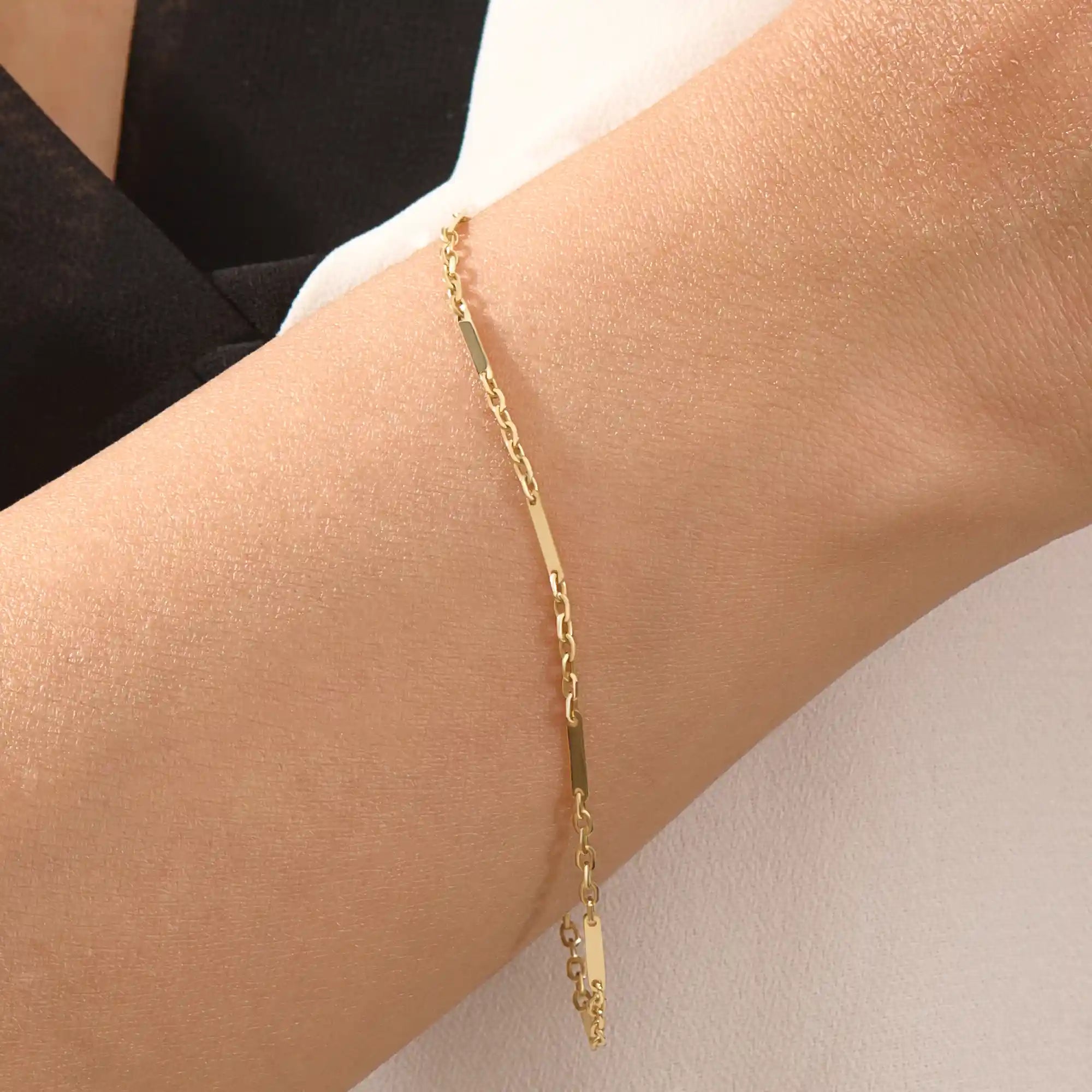 Close-up of a woman wearing a 14k solid yellow gold flat bar chain bracelet, the delicate design draping elegantly across the wrist for a timeless minimalist look.