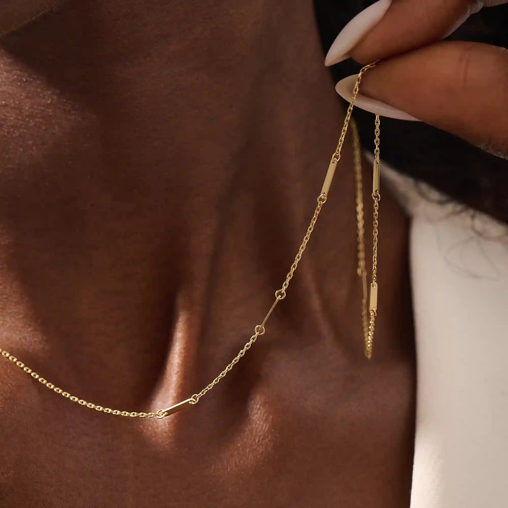 Close-up of a woman wearing a 14k solid yellow gold flat bar chain necklace with evenly spaced polished rectangular accents, styled alone for a refined, modern statement.