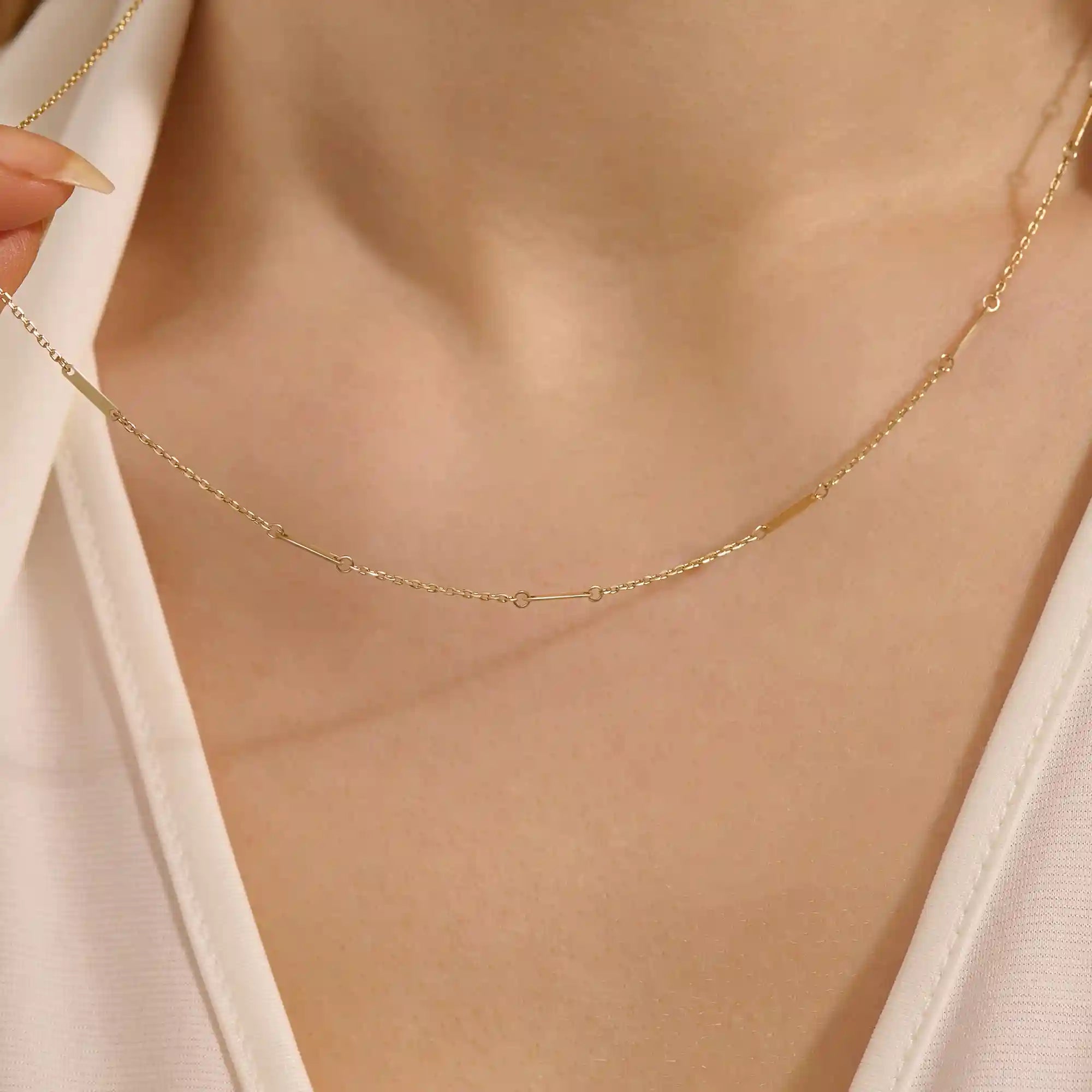 Close-up of a woman wearing a 14k solid yellow gold flat bar chain necklace with evenly spaced polished rectangular accents, styled alone for a refined, modern statement.