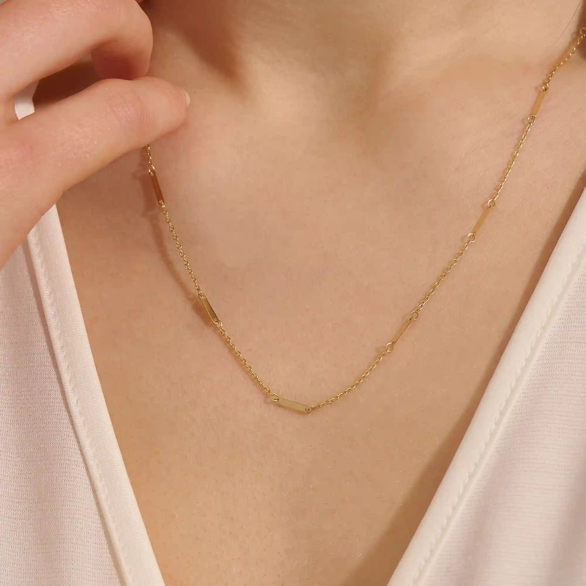 Close-up of a woman wearing a 14k solid yellow gold flat bar chain necklace with evenly spaced polished rectangular accents, styled alone for a refined, modern statement.