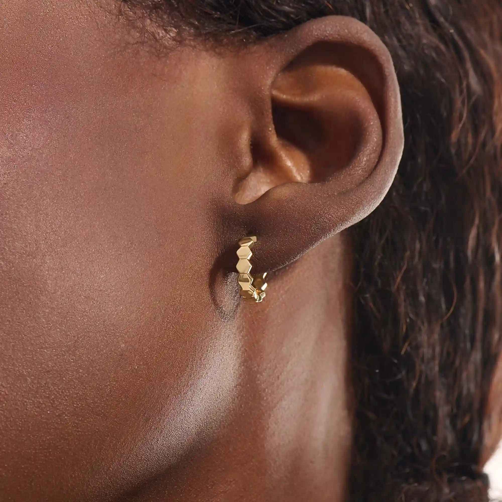 Close-up of a woman wearing a 14k solid yellow gold hexagon hoop earring, its geometric links catching the light with each movement.