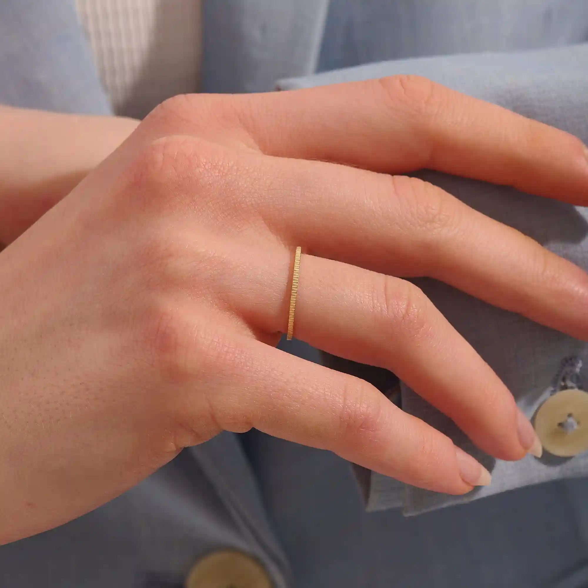 Close-up of a woman wearing a 14k solid yellow gold thin stacking ring with faceted textured design, minimal and elegant everyday jewelry
