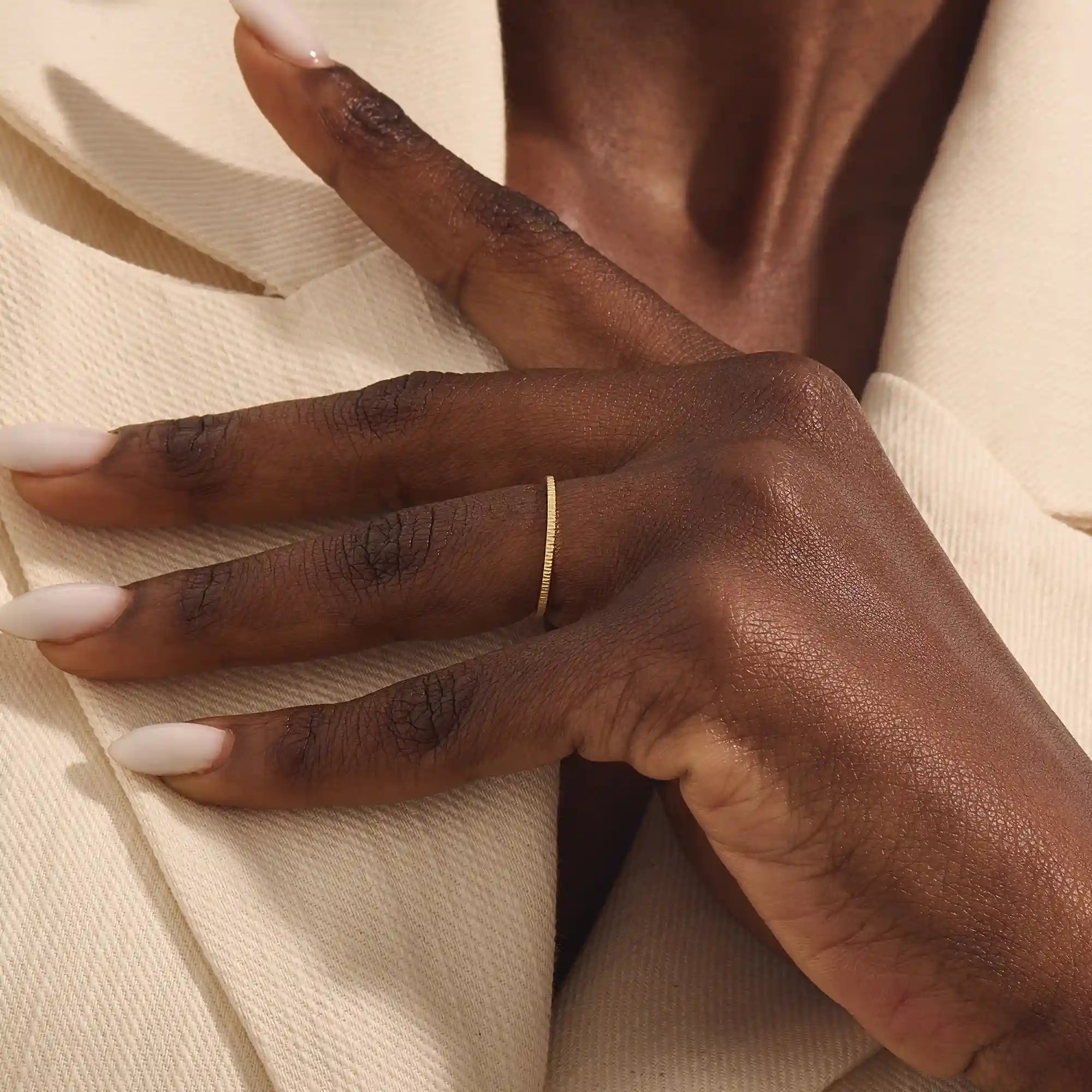 Close-up of a woman wearing a 14k solid yellow gold thin stacking ring with faceted textured design, minimal and elegant everyday jewelry