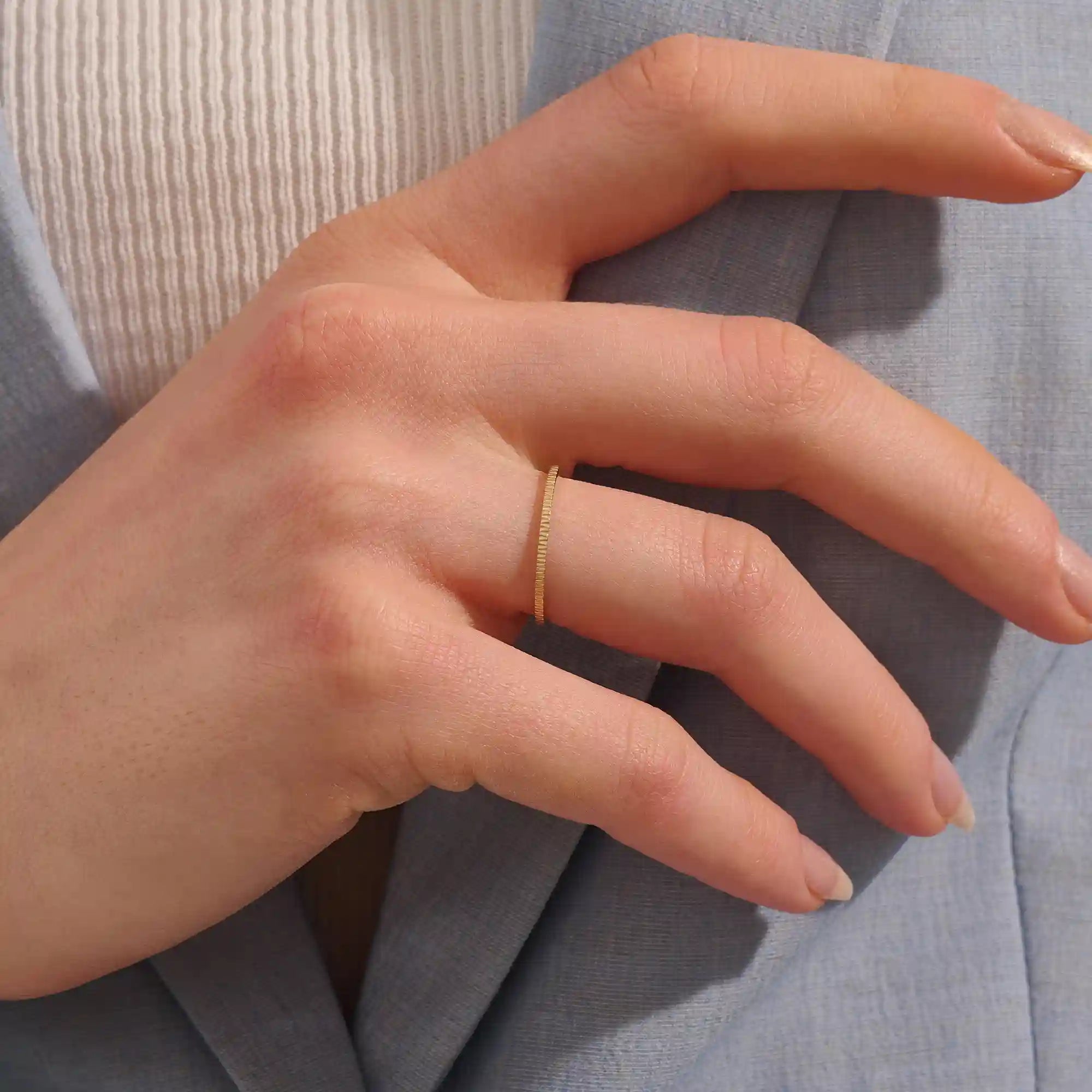 Close-up of a woman wearing a 14k solid yellow gold thin stacking ring with faceted textured design, minimal and elegant everyday jewelry