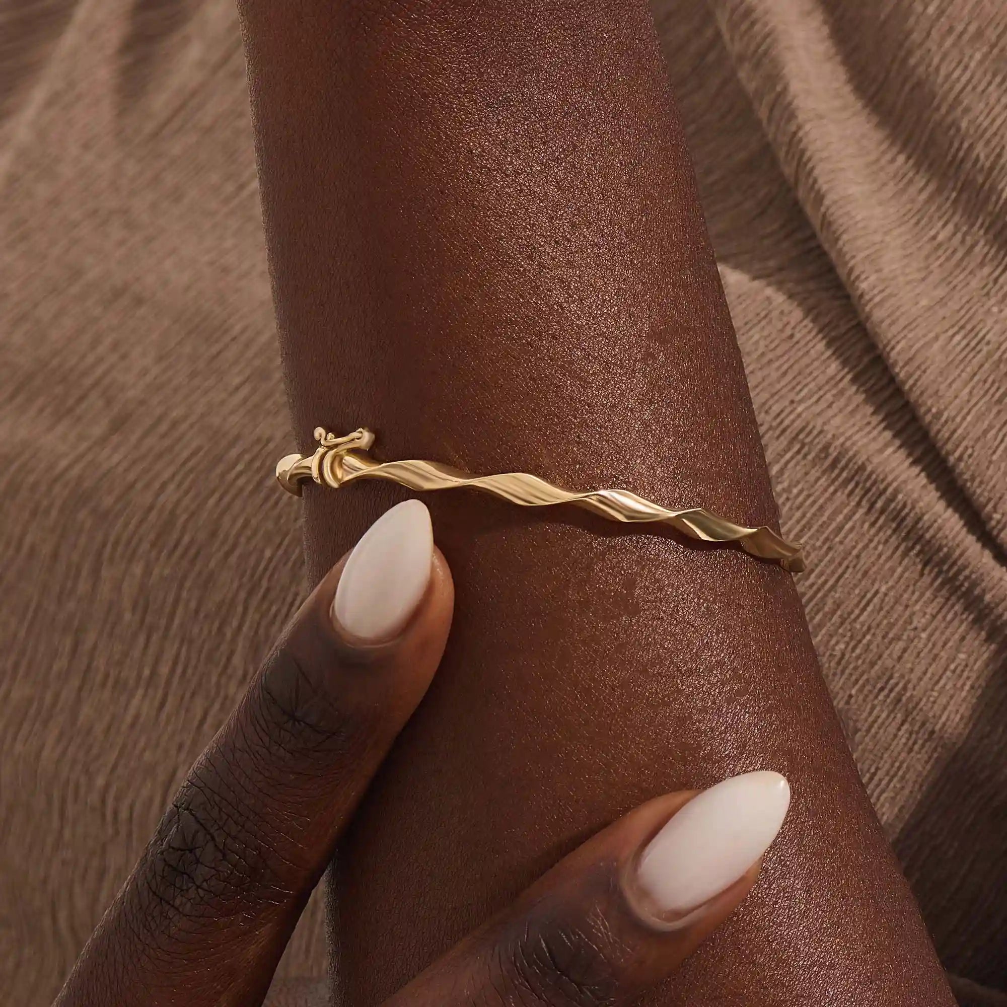 Close-up of a woman wearing a 14k solid yellow gold twist bangle bracelet, showing the bracelet’s sculpted wave design glimmering in natural light.