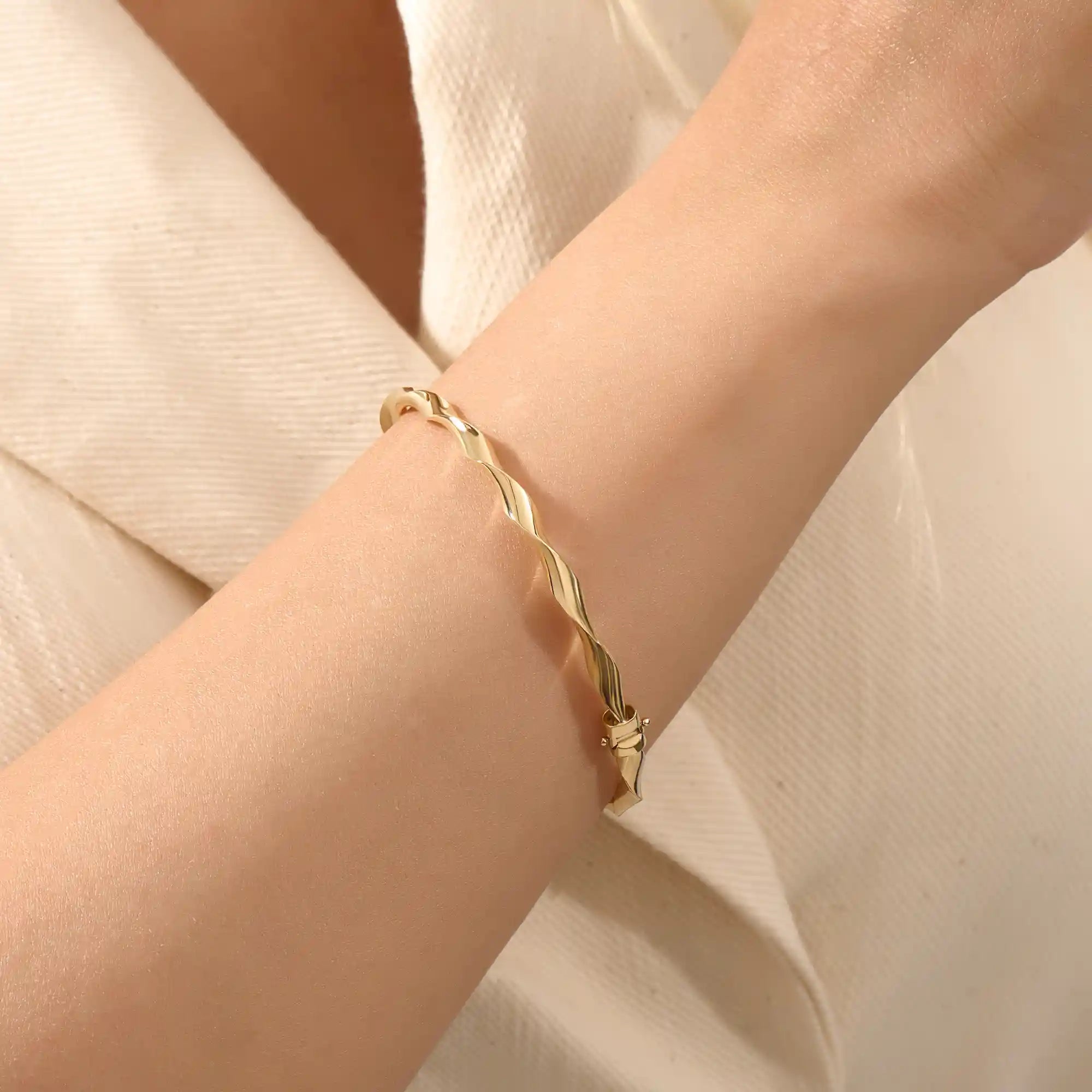 Close-up of a woman wearing a 14k solid yellow gold twist bangle bracelet, showing the bracelet’s sculpted wave design glimmering in natural light.