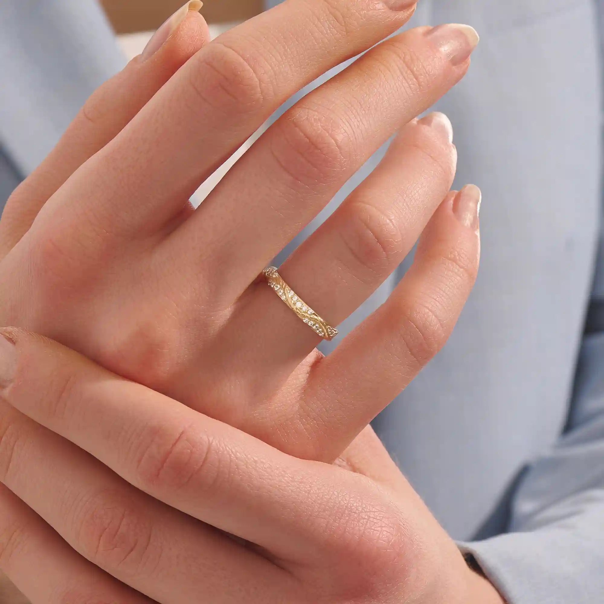 Close-up of a woman wearing a 14k solid yellow gold twisted eternity wedding band with sparkling moissanites in a continuous setting
