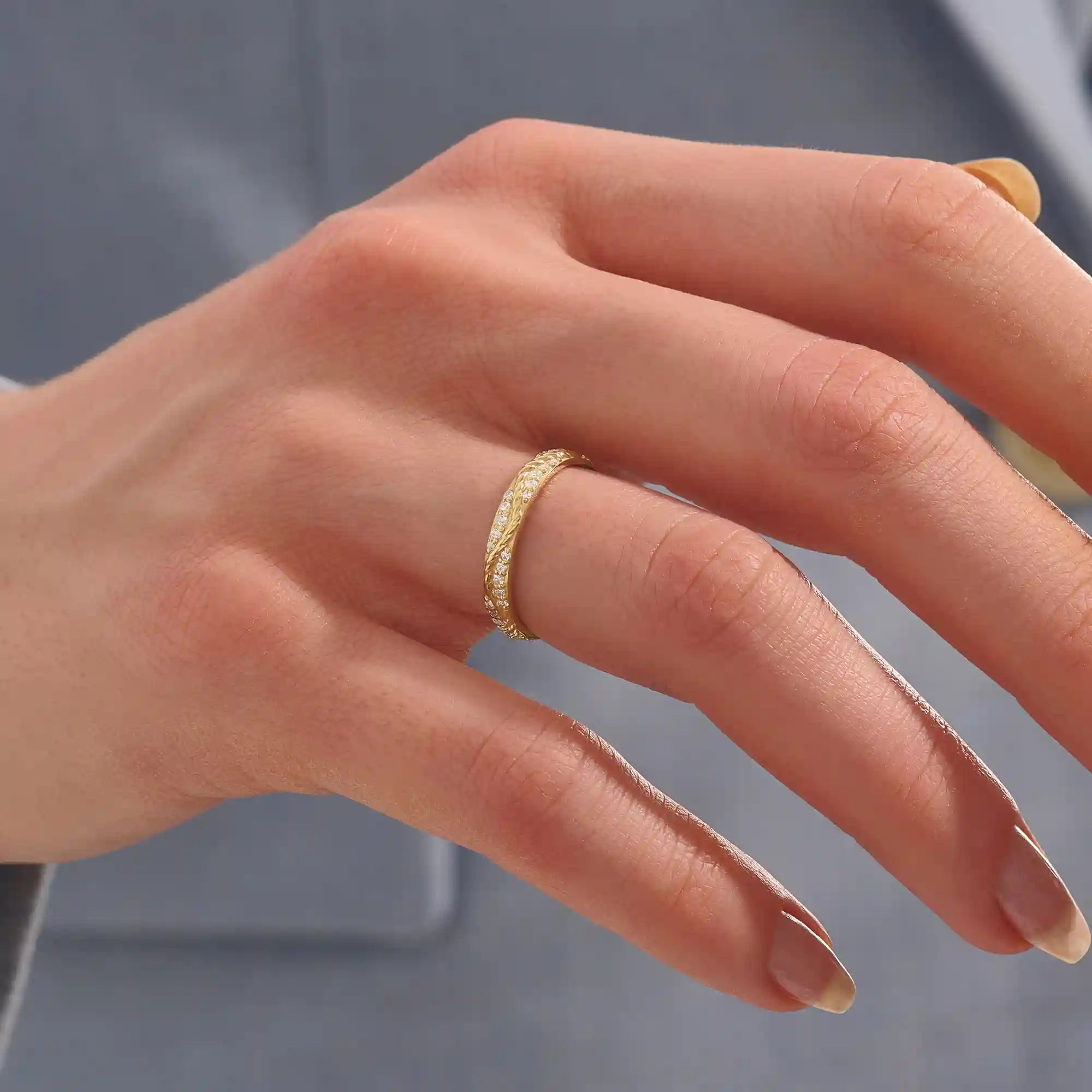 Close-up of a woman wearing a 14k solid yellow gold twisted eternity wedding band with sparkling moissanites in a continuous setting