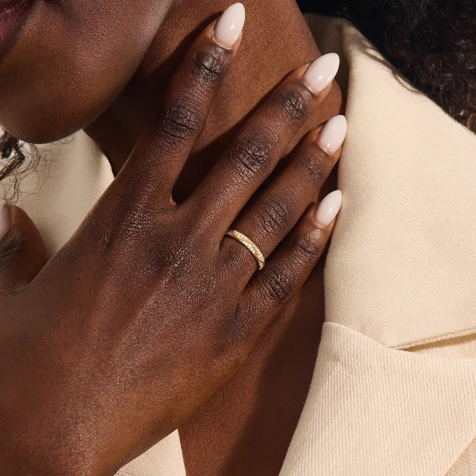 Close-up of a woman wearing a 14k solid yellow gold twisted eternity wedding band with sparkling moissanites in a continuous setting