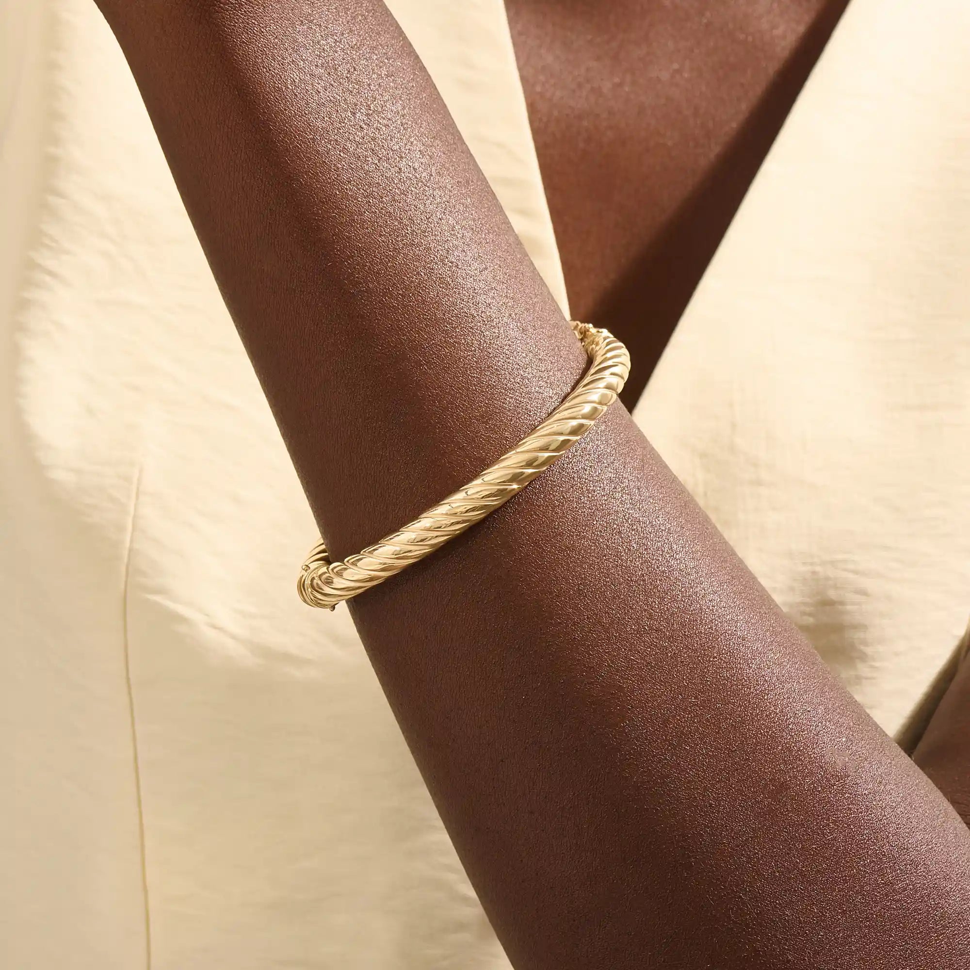 Close-up of a woman wearing a 14k solid yellow gold twisted rope bangle, styled alone to highlight its bold, sculptural form and gleaming polish.