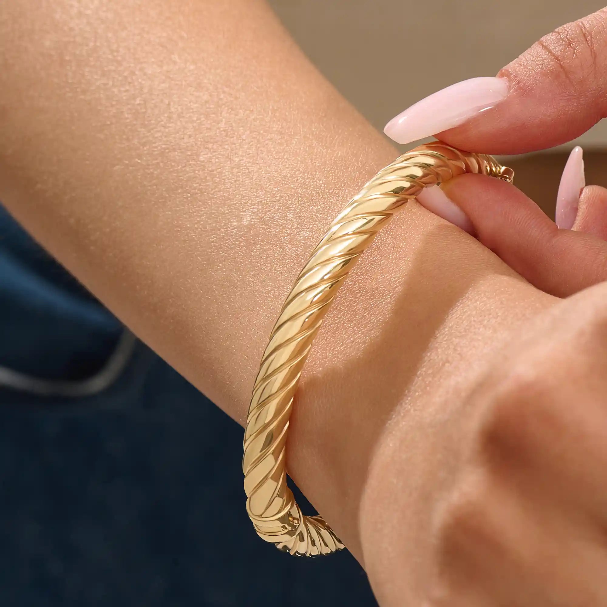 Close-up of a woman wearing a 14k solid yellow gold twisted rope bangle, styled alone to highlight its bold, sculptural form and gleaming polish.