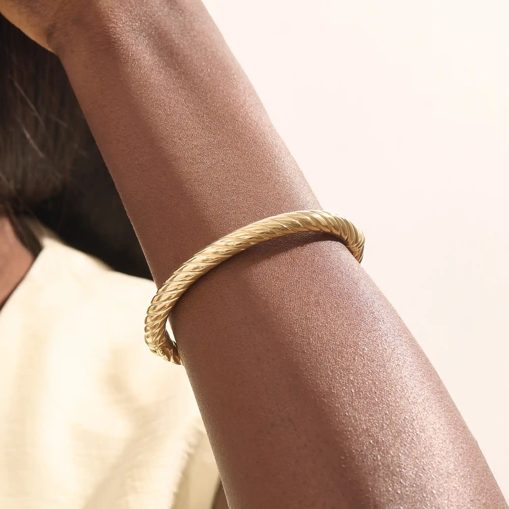 Close-up of a woman wearing a 14k solid yellow gold twisted rope bangle, styled alone to highlight its bold, sculptural form and gleaming polish.