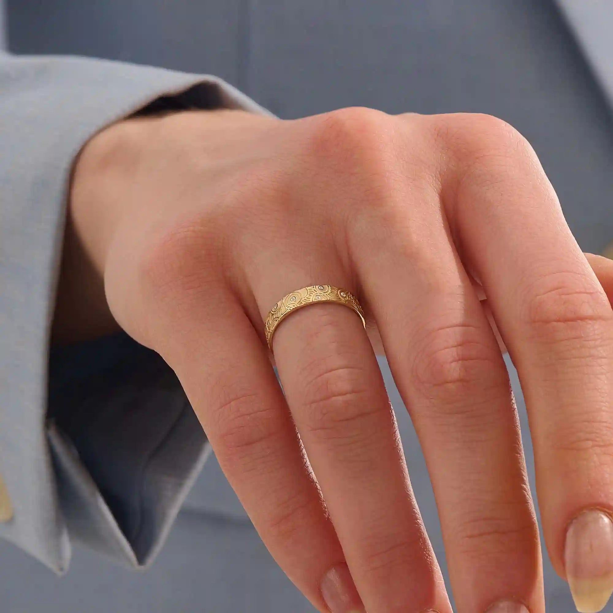 Close-up of a woman wearing a 14k solid yellow gold wedding band with a concentric circle design and bezel-set round moissanites, stylish and distinctive