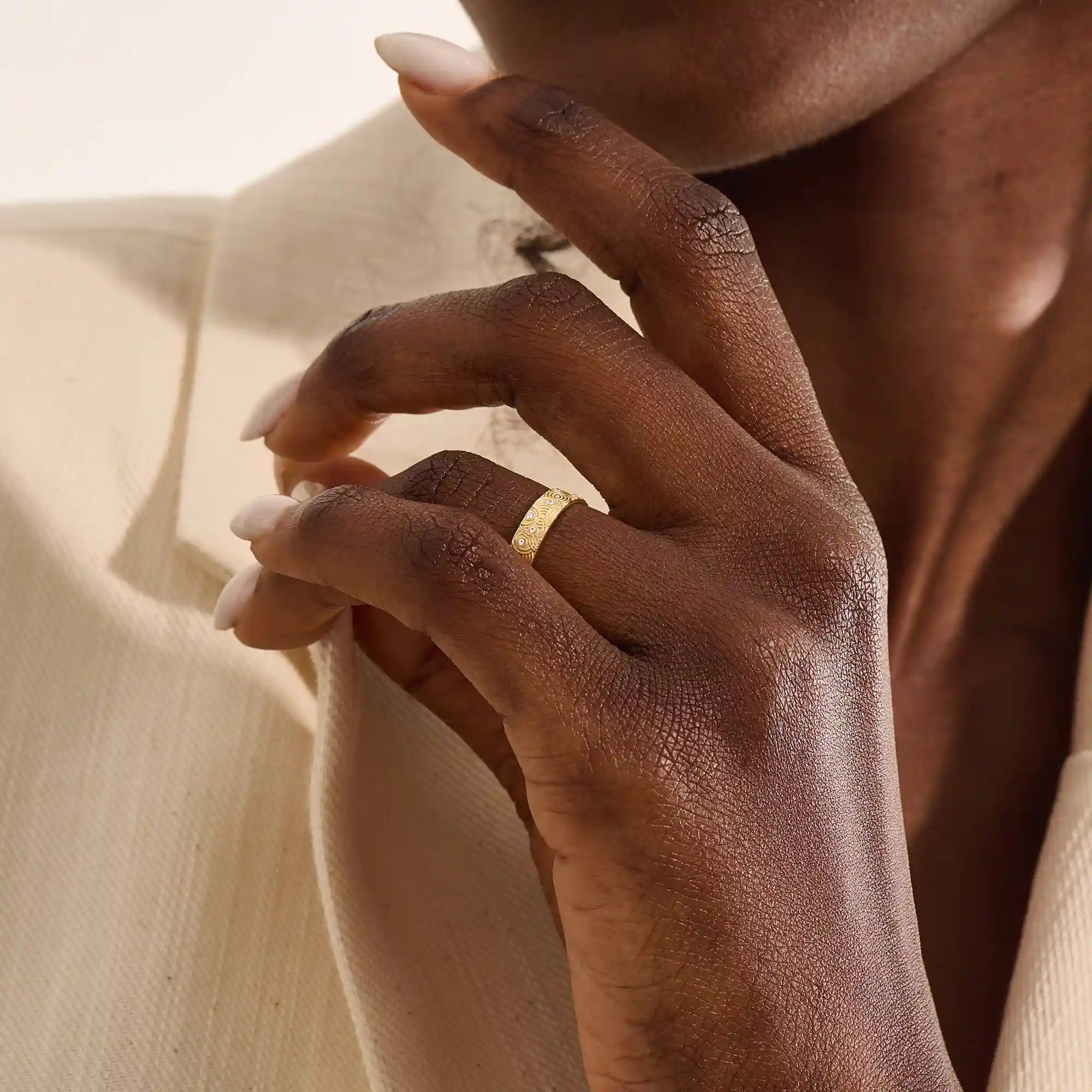 Close-up of a woman wearing a 14k solid yellow gold wedding band with a concentric circle design and bezel-set round moissanites, stylish and distinctive