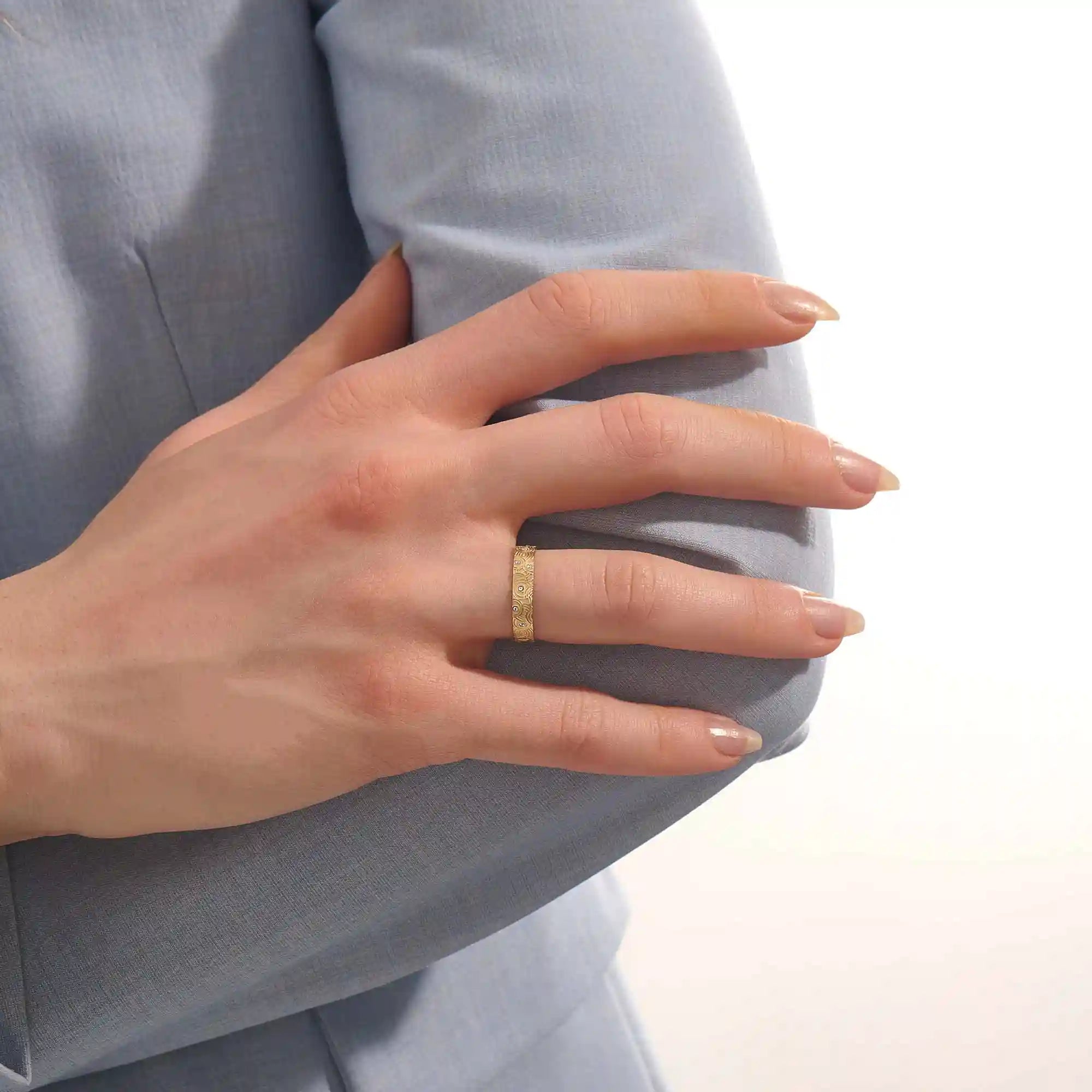 Close-up of a woman wearing a 14k solid yellow gold wedding band with a concentric circle design and bezel-set round moissanites, stylish and distinctive