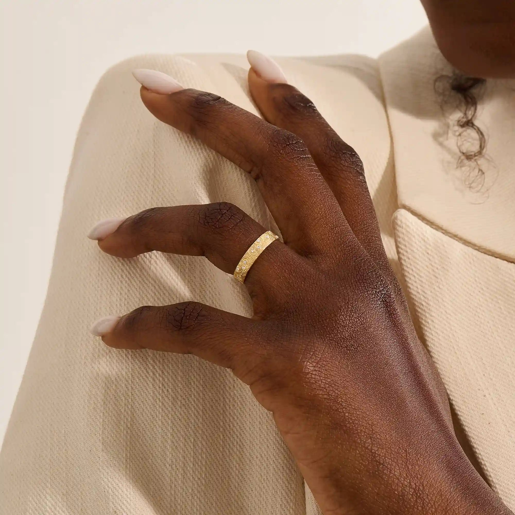 Close-up of a woman wearing a 14k solid yellow gold wedding band with a concentric circle design and bezel-set round moissanites, stylish and distinctive
4
