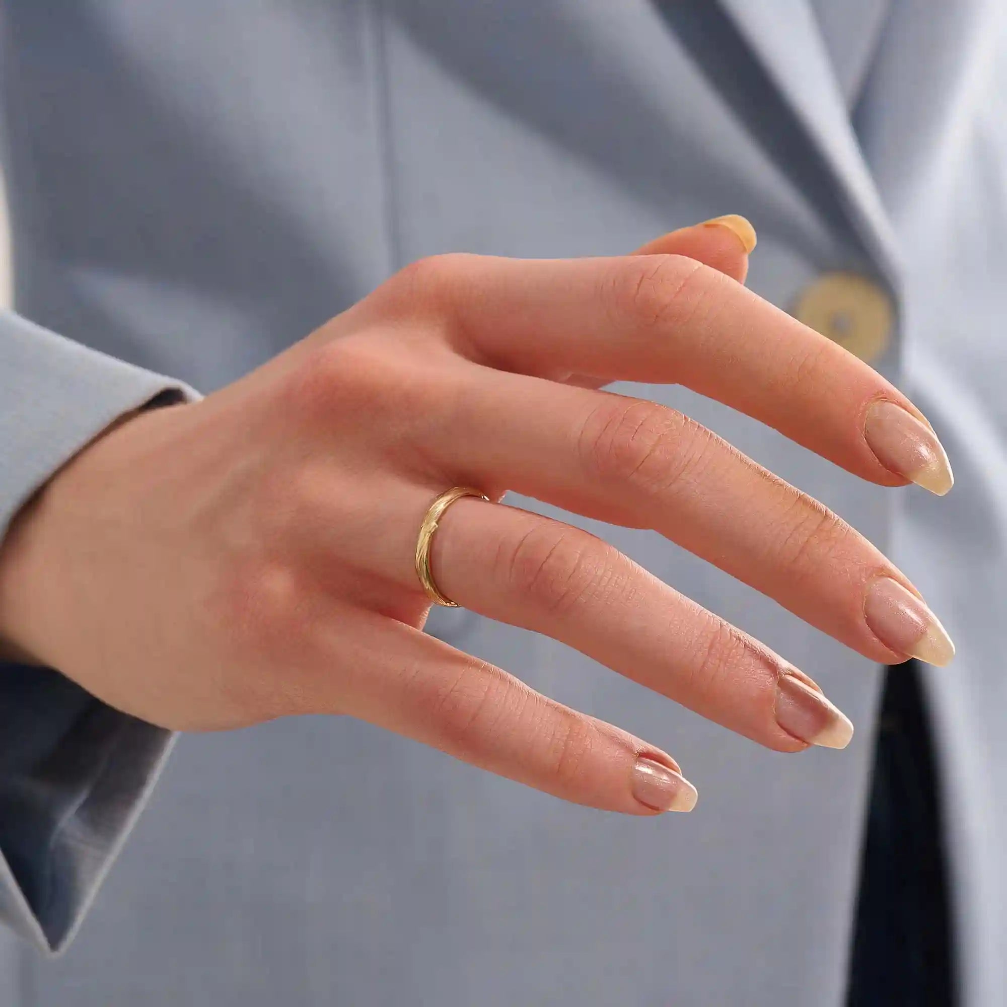 Close-up of a woman wearing a 14k solid yellow gold wedding band with a woodgrain texture, understated and organic style
