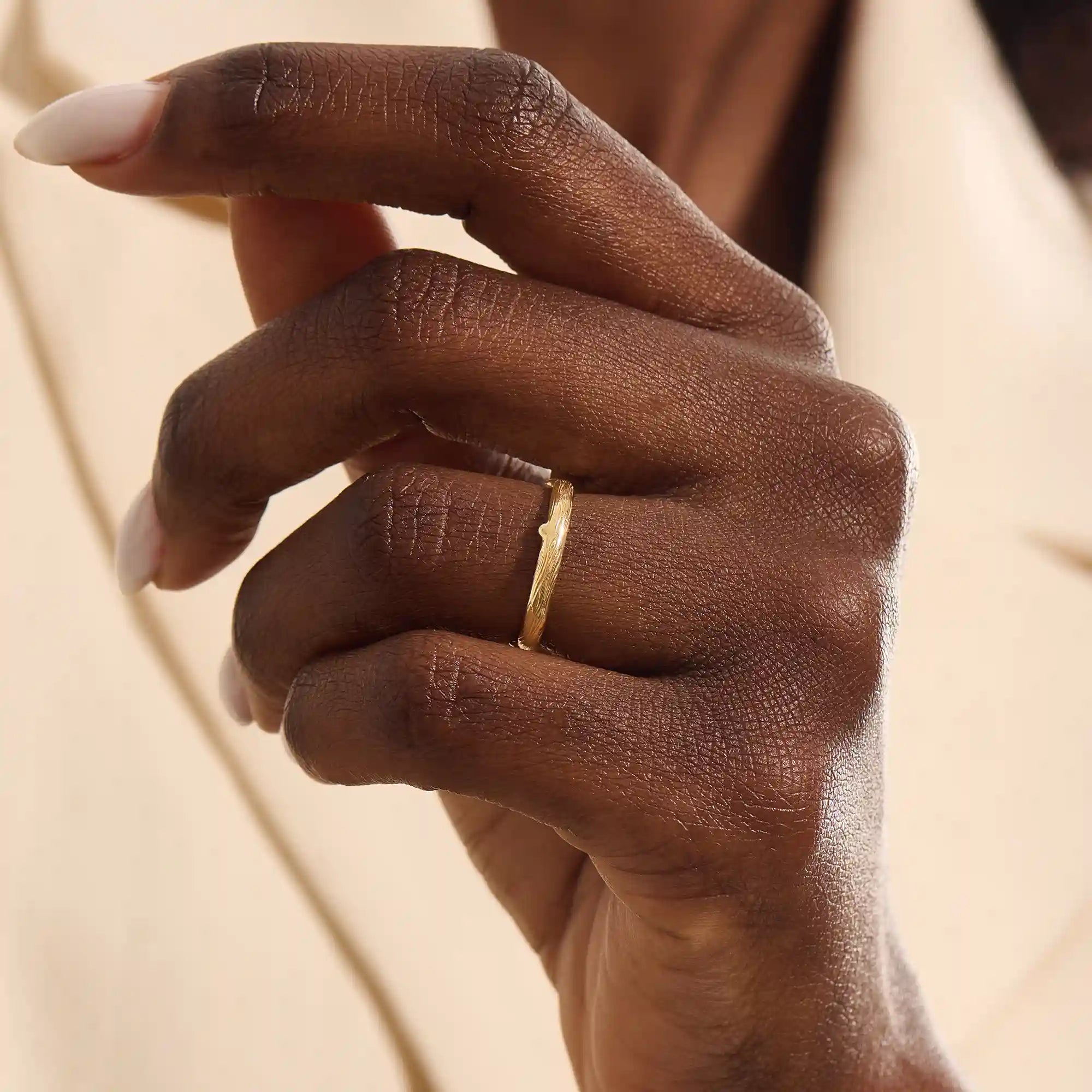 Close-up of a woman wearing a 14k solid yellow gold wedding band with a woodgrain texture, understated and organic style