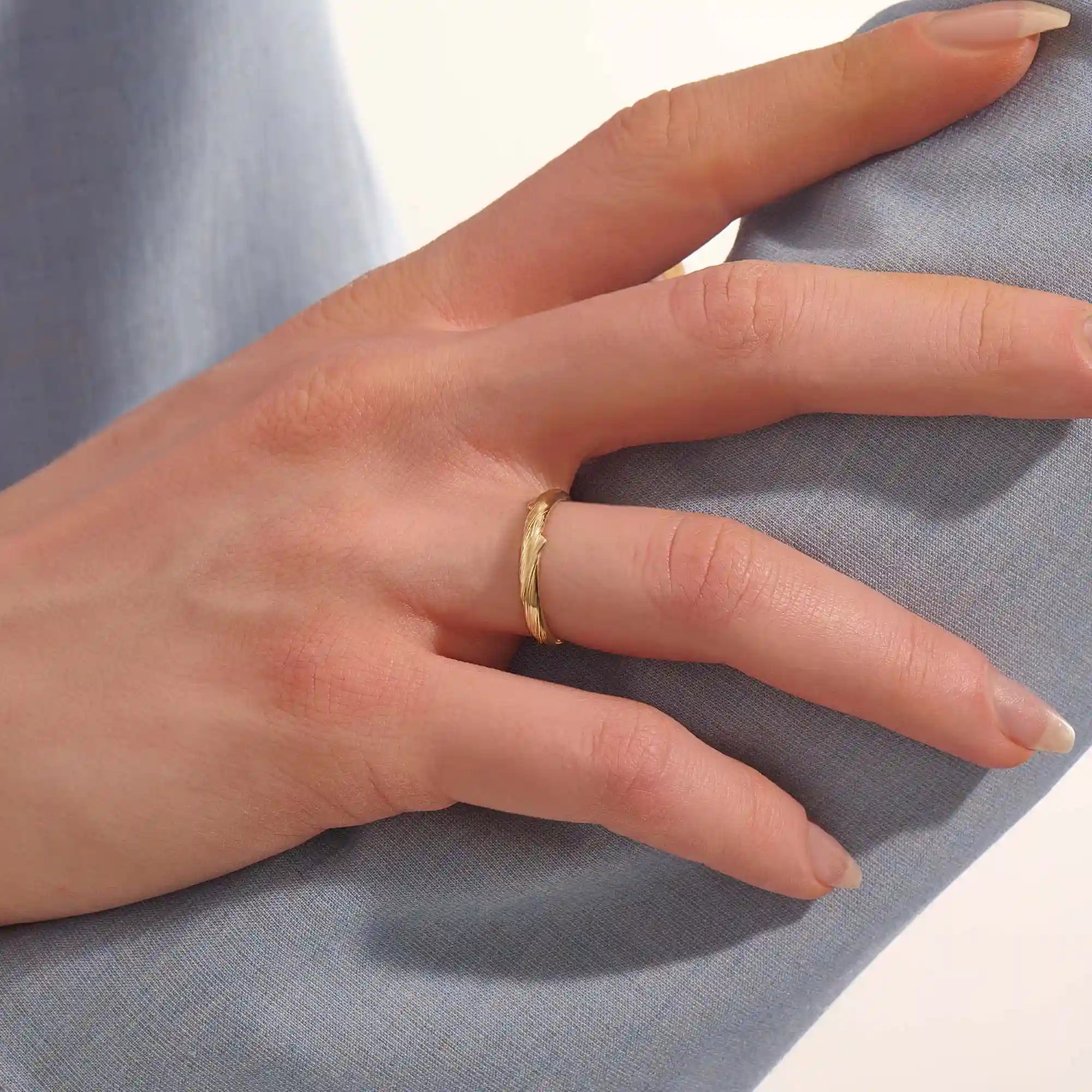 Close-up of a woman wearing a 14k solid yellow gold wedding band with a woodgrain texture, understated and organic style
