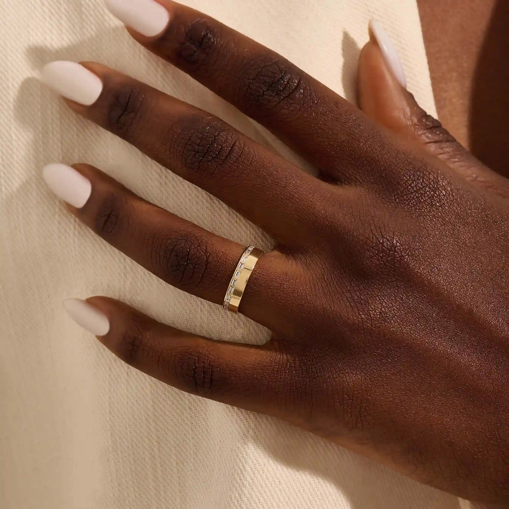 Close-up of a woman wearing a 14k solid yellow gold wide wedding band with baguette moissanite stones in an eternity design