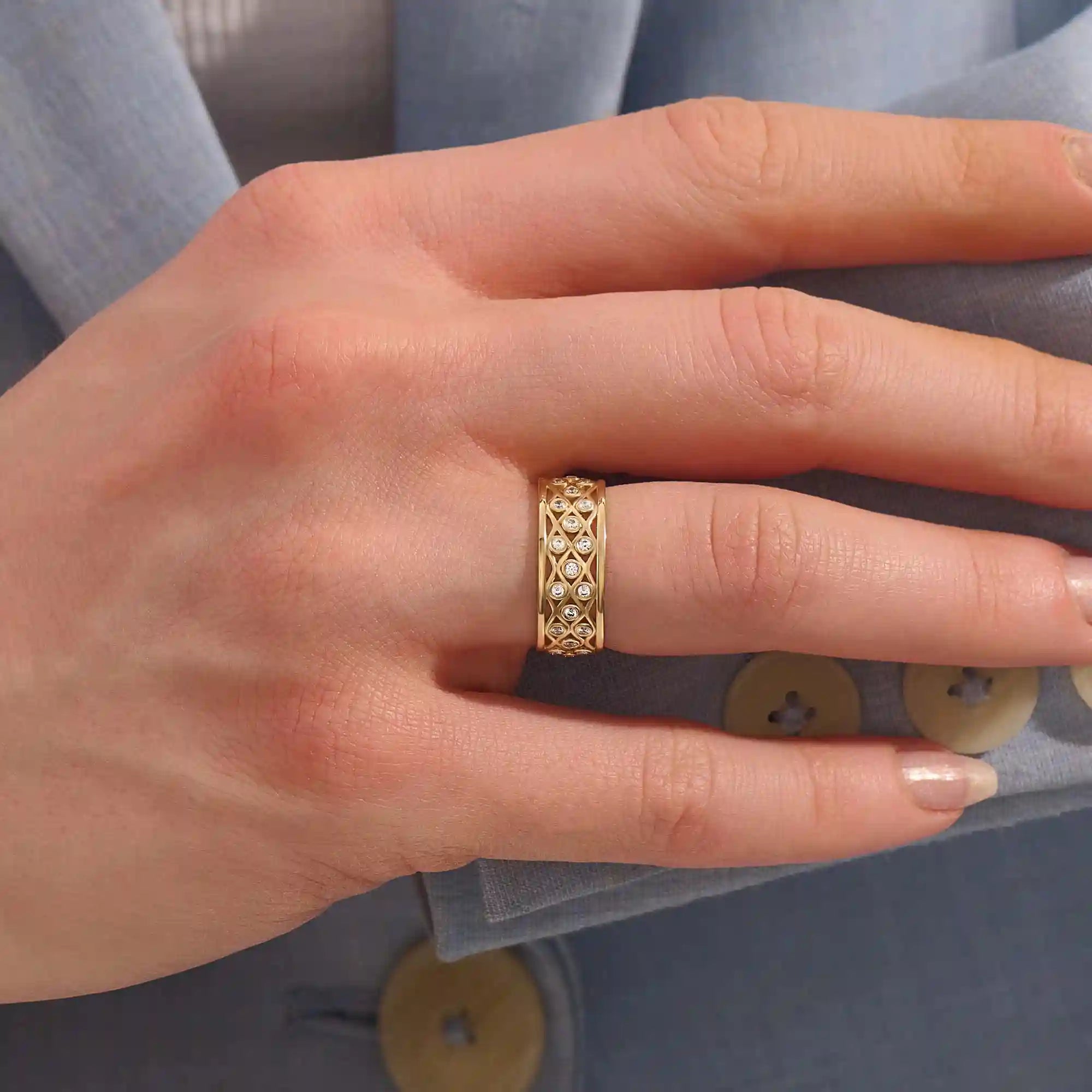 Close-up of a woman wearing a 14k solid yellow gold wide wedding band with moissanite stones in an open lattice setting
