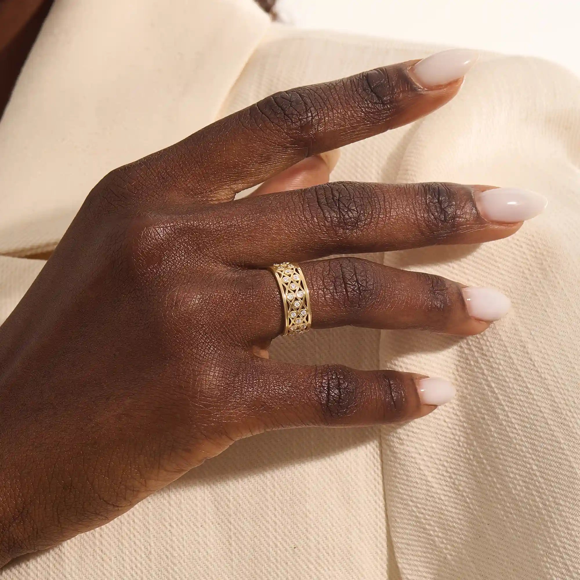 Close-up of a woman wearing a 14k solid yellow gold wide wedding band with moissanite stones in an open lattice setting