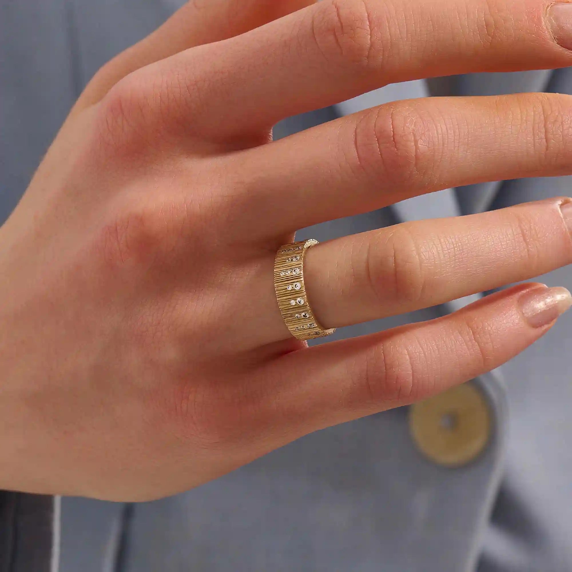 Close-up of a woman wearing a 14k solid yellow gold wide wedding band with wood grain texture and pavé set round brilliant cut moissanite stones, distinctive and modern statement jewelry
